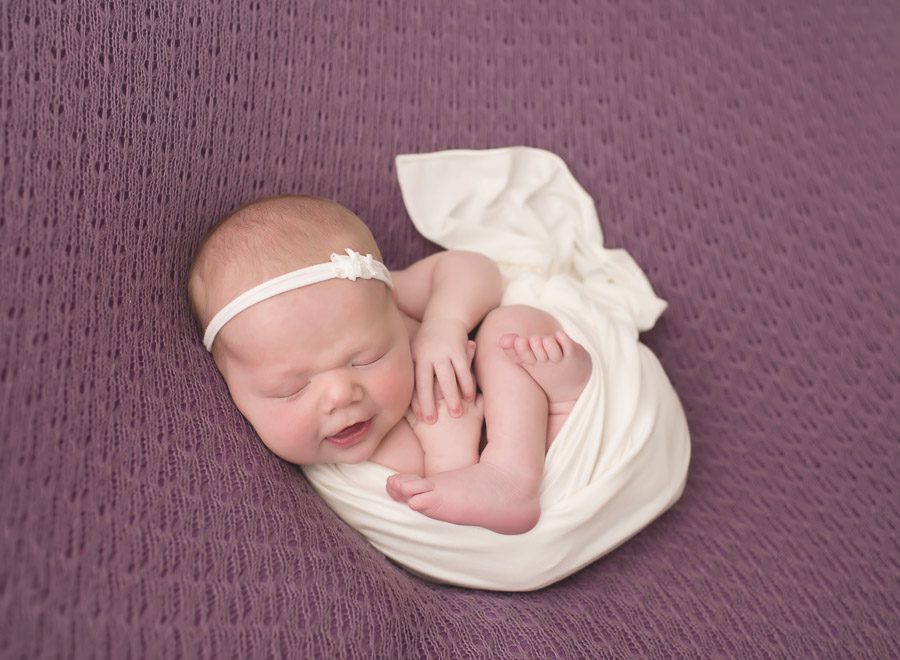 Melissa Hartigan Photography Best Connecticut Newborn Photographer baby wrapped in white smiling wearing a dainty headband