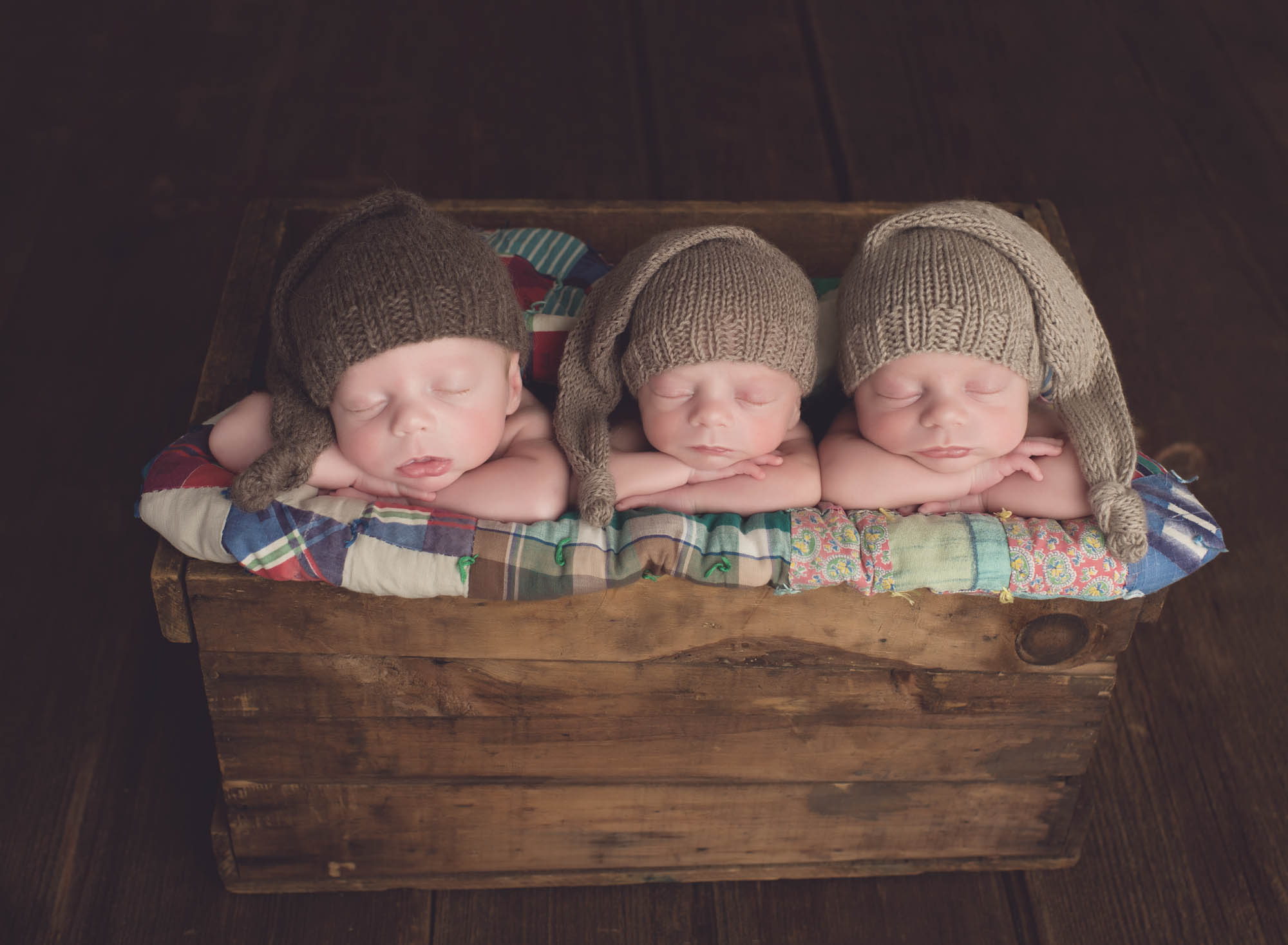 3 new baby boys posed in crate with chin on hands wearing sleepy caps Connecticut Newborn Photographer