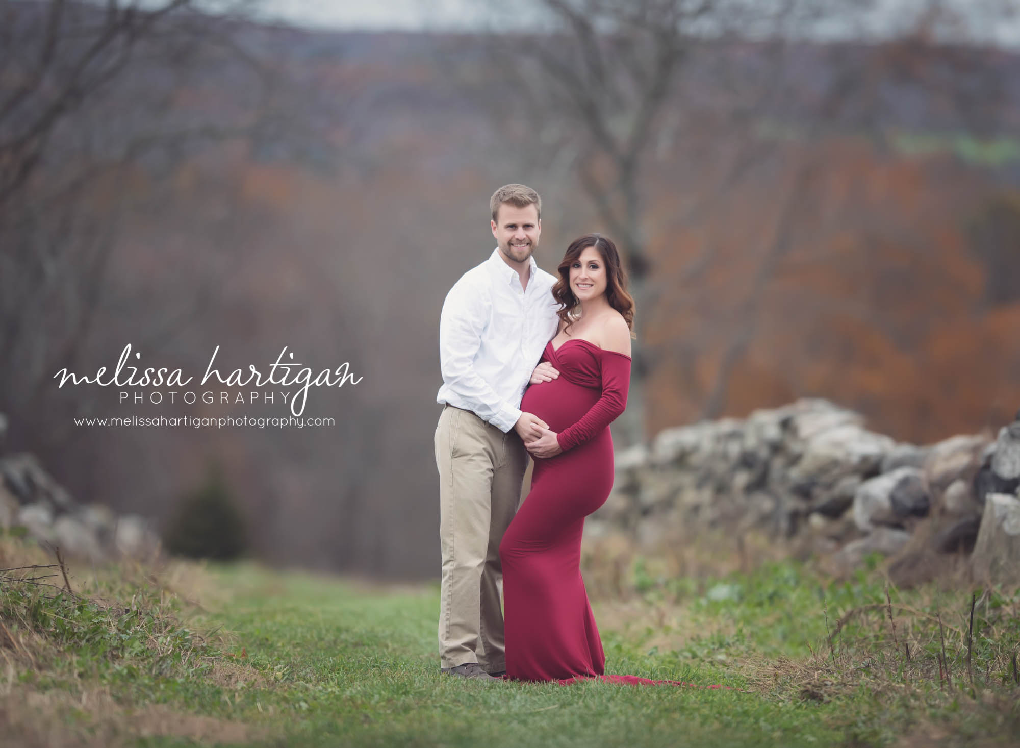 Melissa Hartigan Photography Coventry CT Newborn & Maternity Photographer Coventry CT Maternity Newborn Session Carrie wearing red maternity gown standing in field with husband holding baby bump