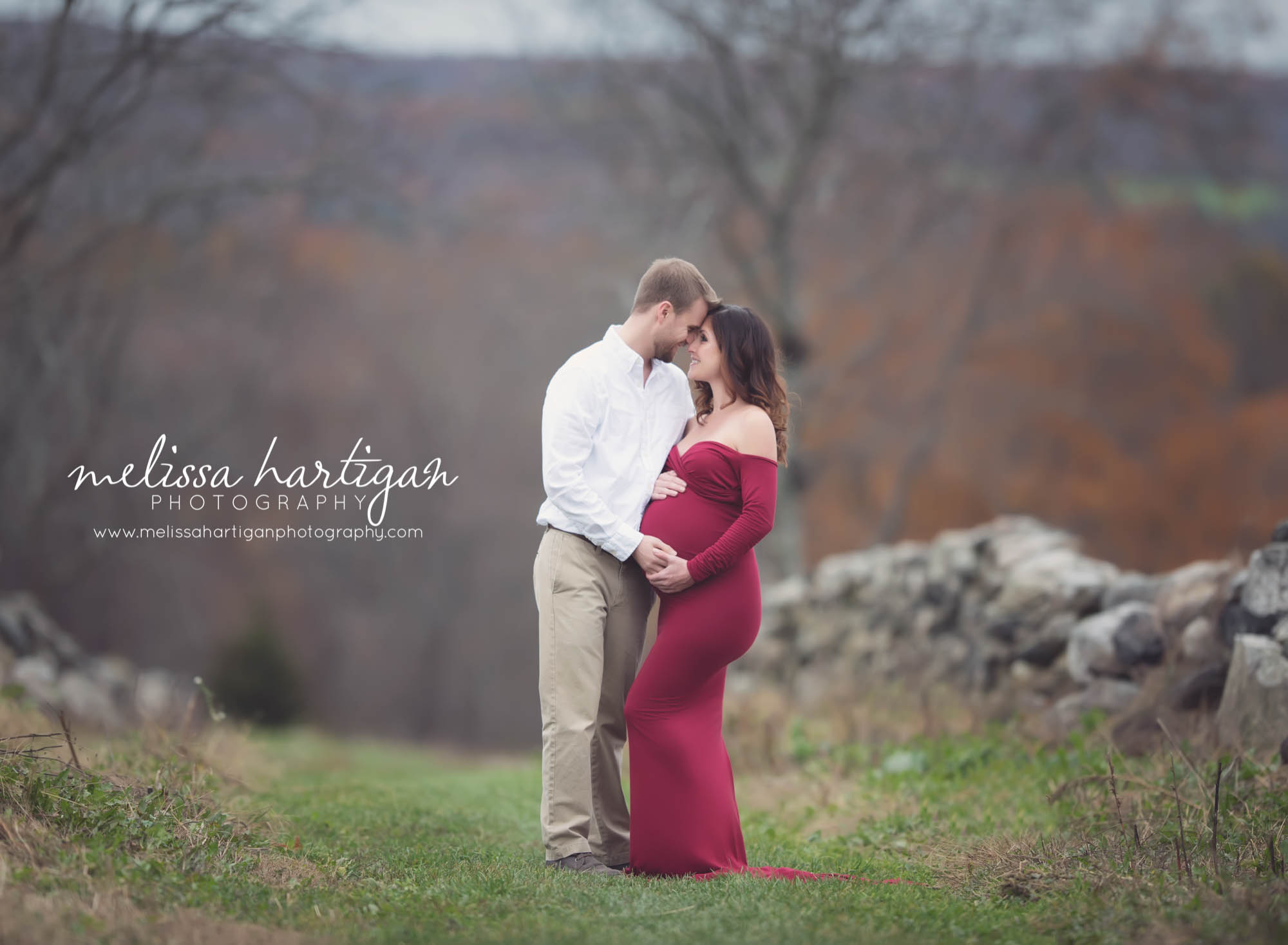 Melissa Hartigan Photography Coventry CT Newborn & Maternity Photographer Coventry CT Maternity Newborn Session Carrie wearing red maternity gown standing in field with husband holding baby bump touching faces