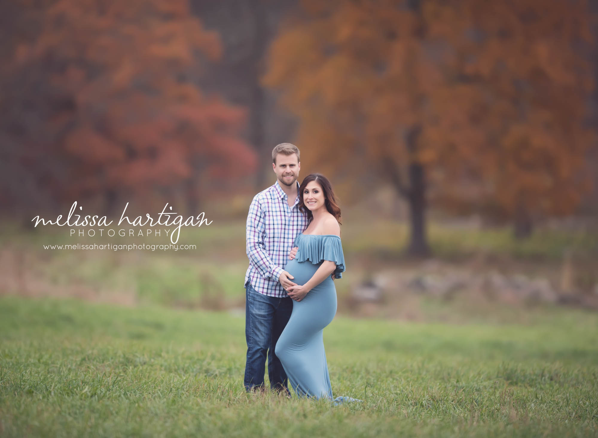 Melissa Hartigan Photography Coventry CT Newborn & Maternity Photographer Coventry CT Maternity Newborn Session Carrie wearing blue maternity gown standing in field holding baby bump with husband