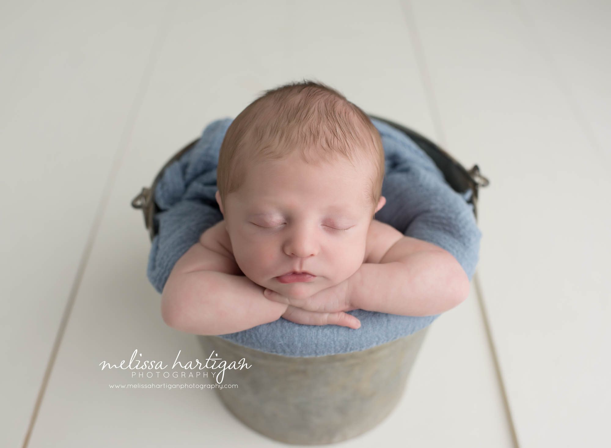 Melissa Hartigan Photography Coventry CT Newborn & Maternity Photographer Coventry CT Maternity Newborn Session Chase sleeping in metal bucket with blue blanket head on hands