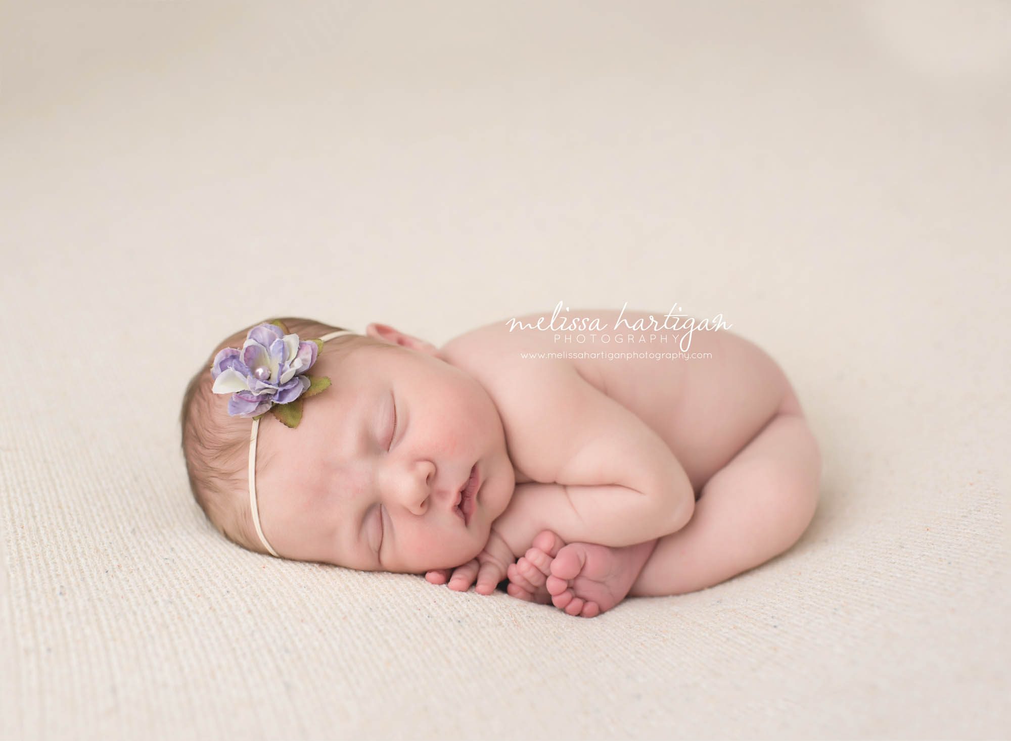 Melissa Hartigan Photography Connecticut Newborn Photographer Coventry Ct Middlefield CT baby Fairfield county Baby girl purple flower headband on pale pink blanket sleeping head on hands CT newborn session