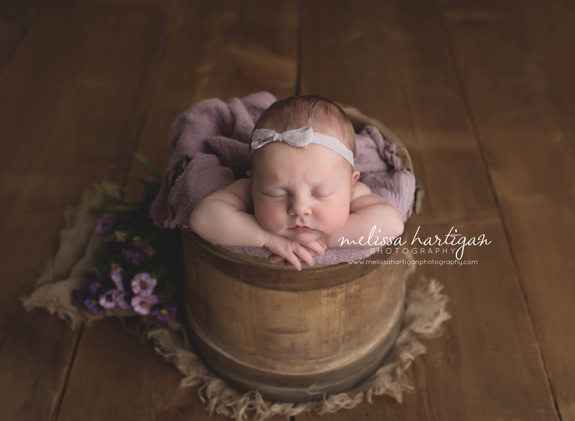 Melissa Hartigan Photography Connecticut Newborn Photographer Coventry Ct Middlefield CT baby Fairfield county Baby girl purple headband and blanket in wooden bucket with purple flowers sleeping CT newborn session