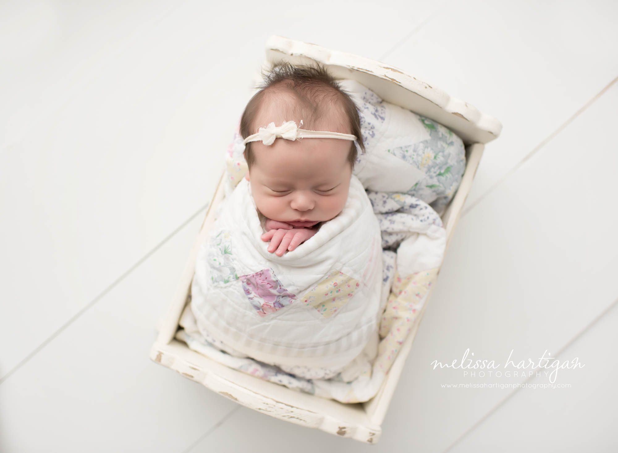 Melissa Hartigan Photography Connecticut Newborn Photographer Coventry Ct Middlefield CT baby Fairfield county Newborn and maternity photography Baby girl cream headband wrapped in patchwork blanket in white wooden bed sleeping