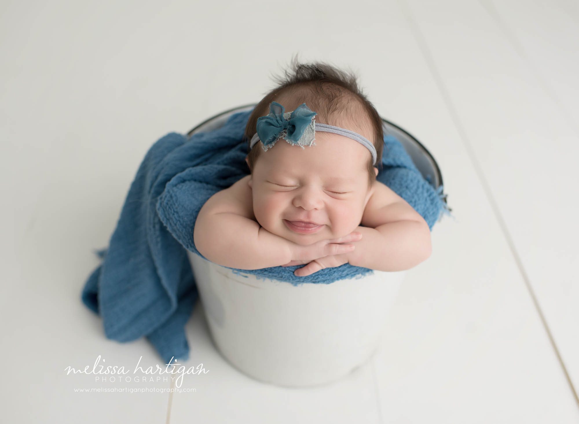 Melissa Hartigan Photography Connecticut Newborn Photographer Coventry Ct Middlefield CT baby Fairfield county Newborn and maternity photography Baby girl blue headband in white metal bucket with blue wrap head on arms smiling sleeping