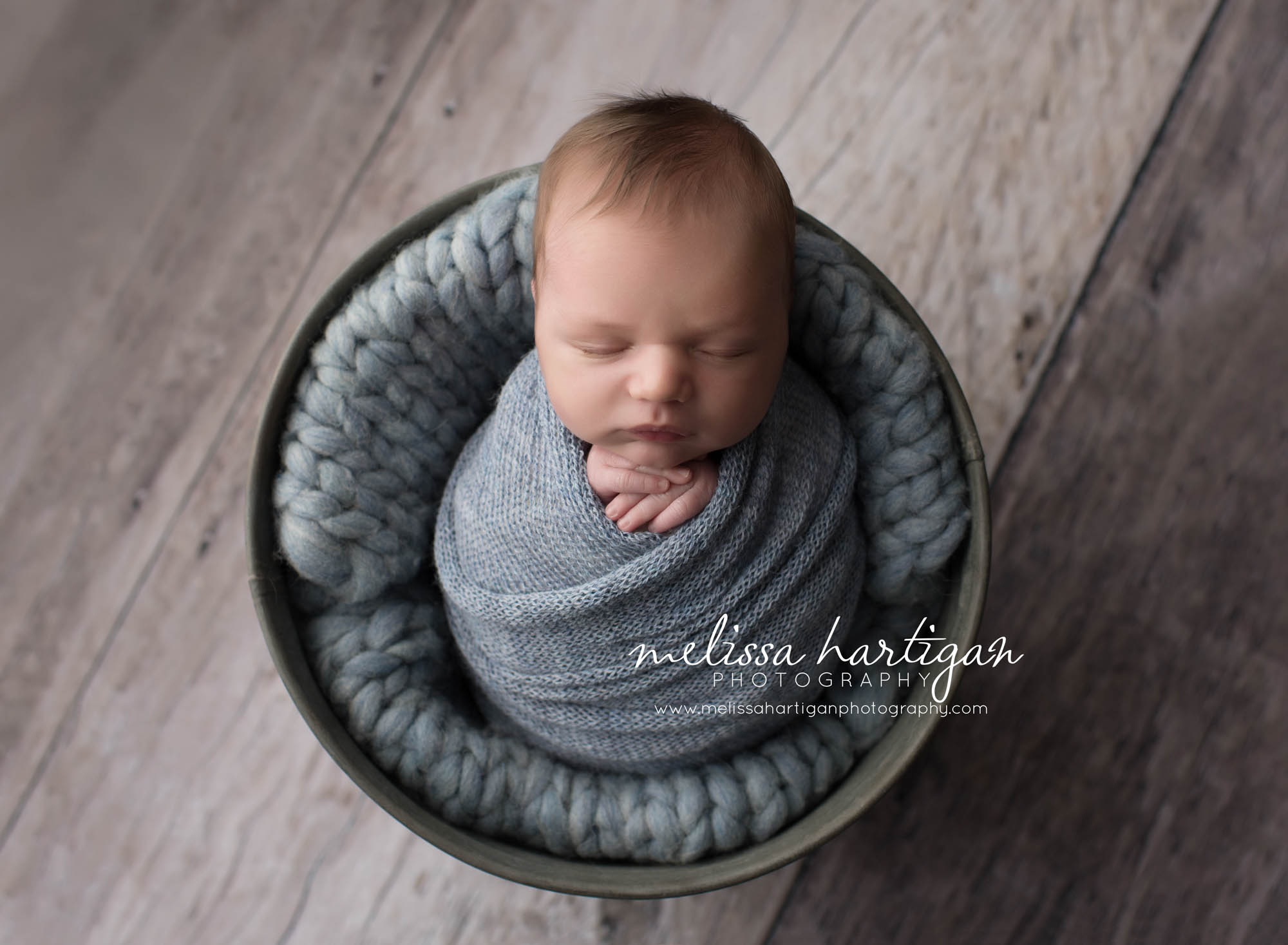 Melissa Hartigan Photography Coventry CT Simply Swaddled Newborn Session baby boy wrapped in blue knit wrap laying on chunky blue blanket in a bucket