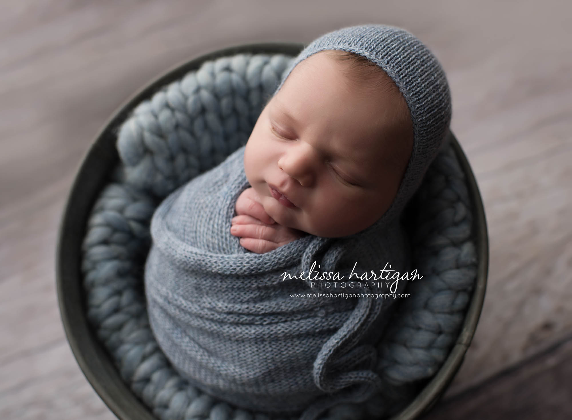 Melissa Hartigan Photography Coventry CT Simply Swaddled Newborn Session baby boy wrapped in blue knit wrap and matching hat laying on chunky blue blanket in a bucket