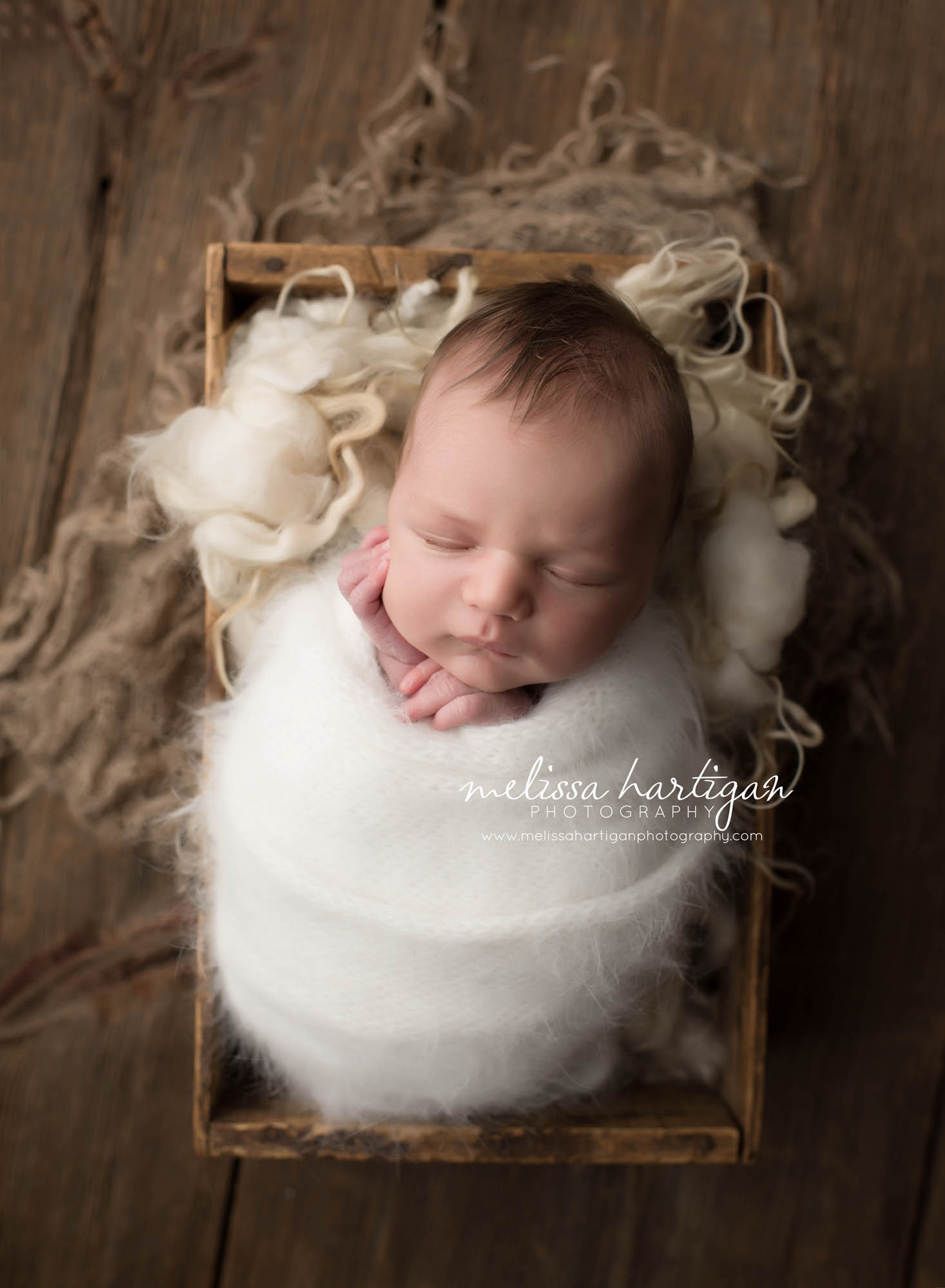 Melissa Hartigan Photography Coventry CT Simply Swaddled Newborn Session baby boy wrapped in white fluffy wrap with hands sticking out sleeping in an antique wooden crate close-up