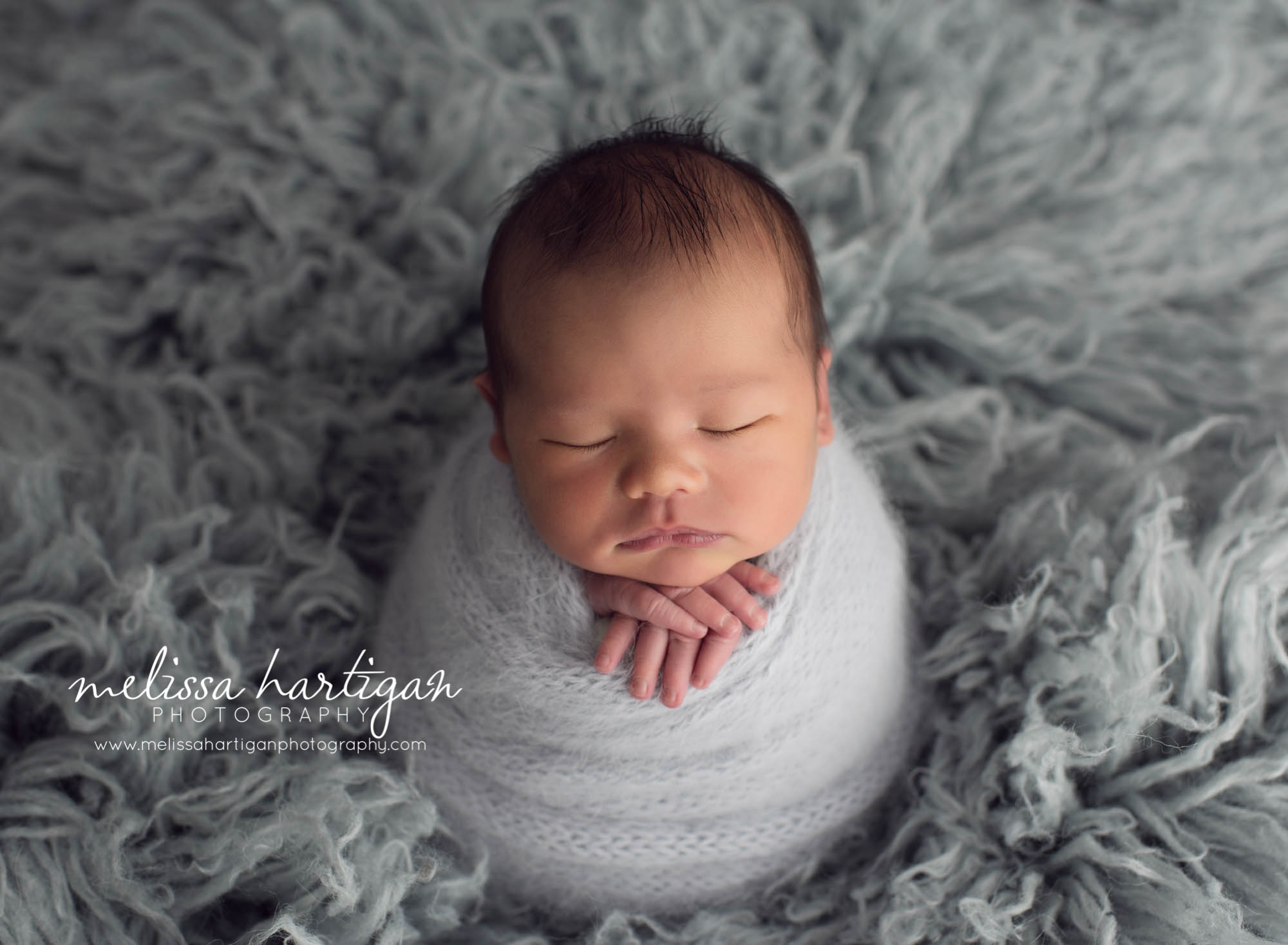 Melissa Hartigan Photography Maternity and Newborn Connecticut Photographer Lucas Newborn Session Baby boy sleeping on light blue knit wrap with hands sticking out on blue flokati