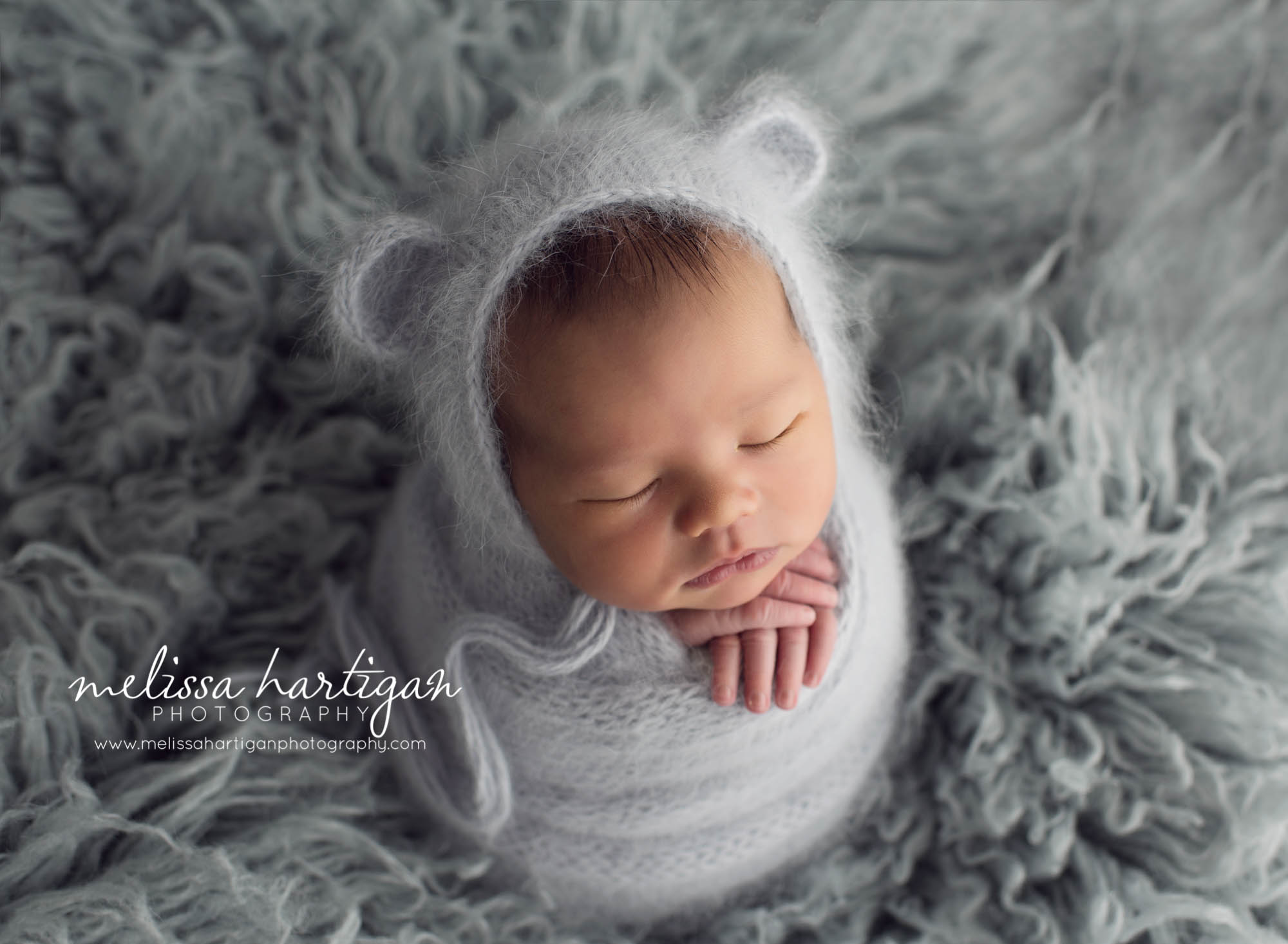 Melissa Hartigan Photography Maternity and Newborn Connecticut Photographer Lucas Newborn Session Baby boy sleeping on light blue knit wrap with hands sticking out wearing hat with ears on blue flokati