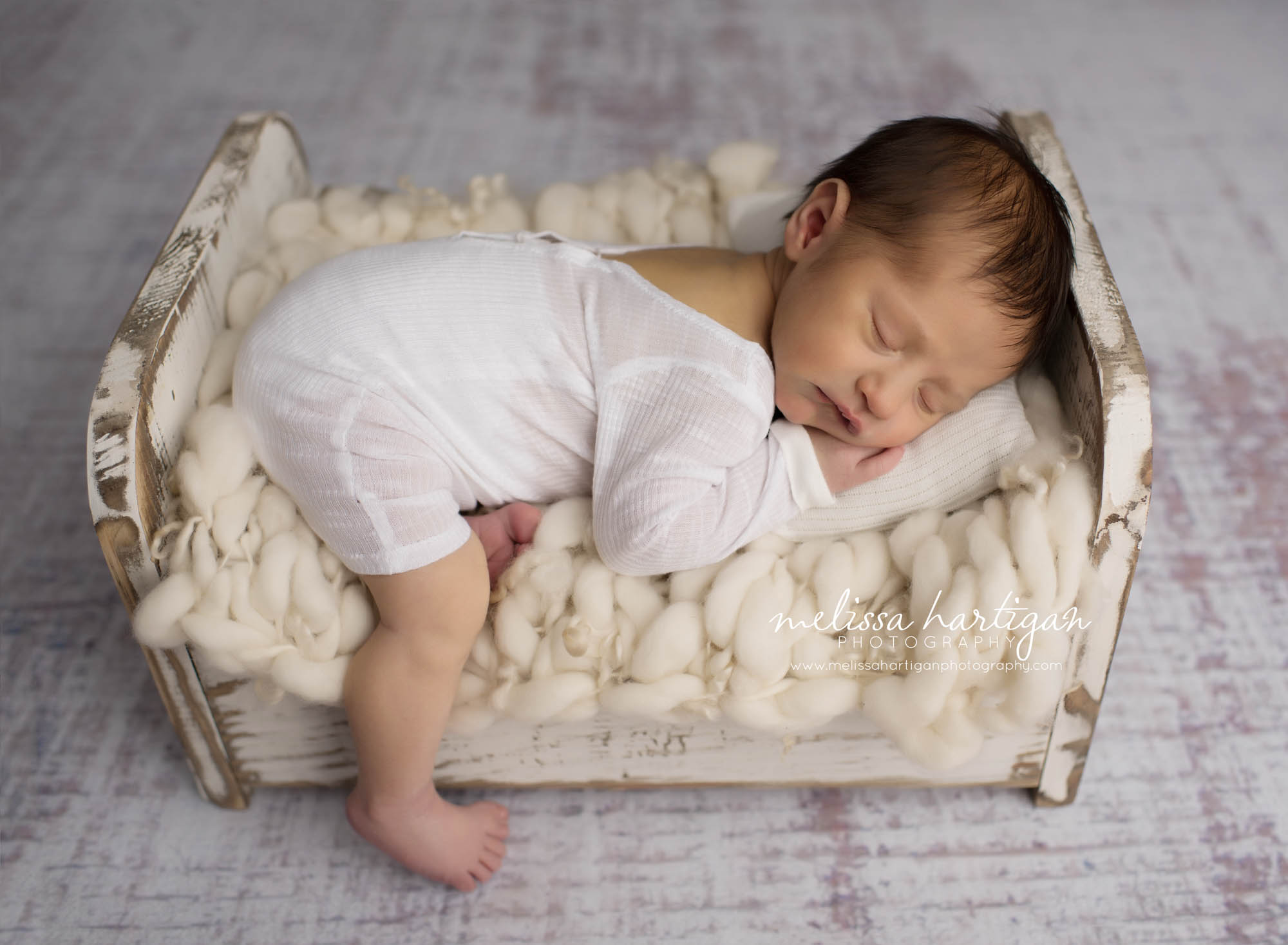 Melissa Hartigan Photography Maternity and Newborn Connecticut Photographer Brayden Mini Newborn Session Baby boy sleeping in antique white bed laying on chunky knit blanket wearing white cotton onesie leg hanging down