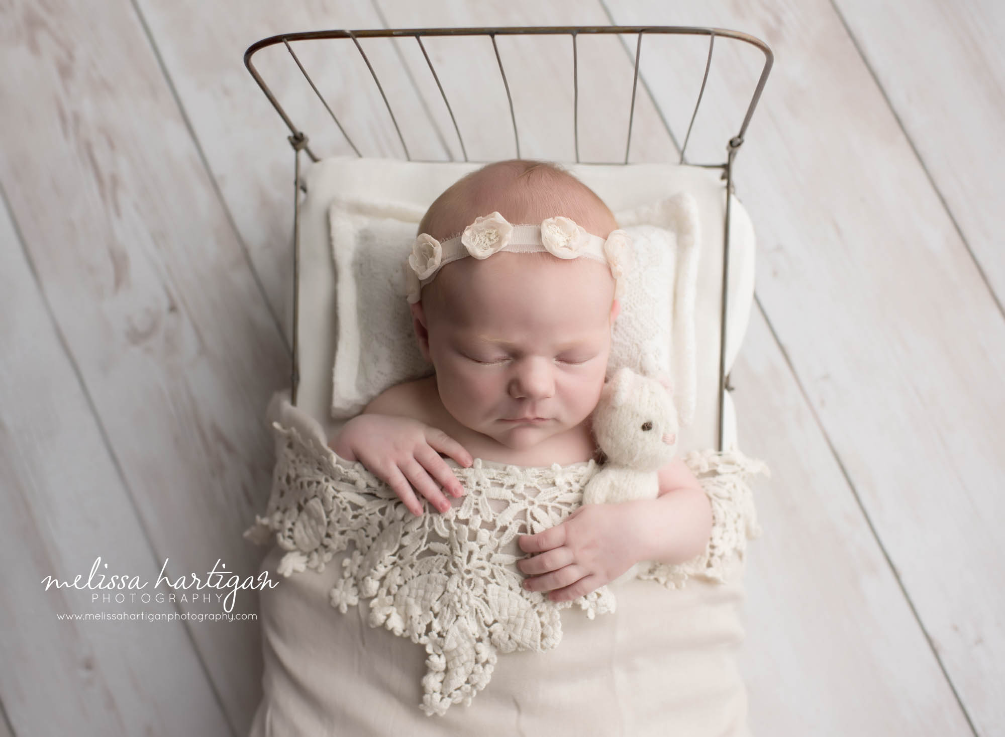 Melissa Hartigan Photography Connecticut Newborn Photographer in Coventry baby girl sleeping in little bed under white lace blanket wearing white floral headband and holding a white little bear