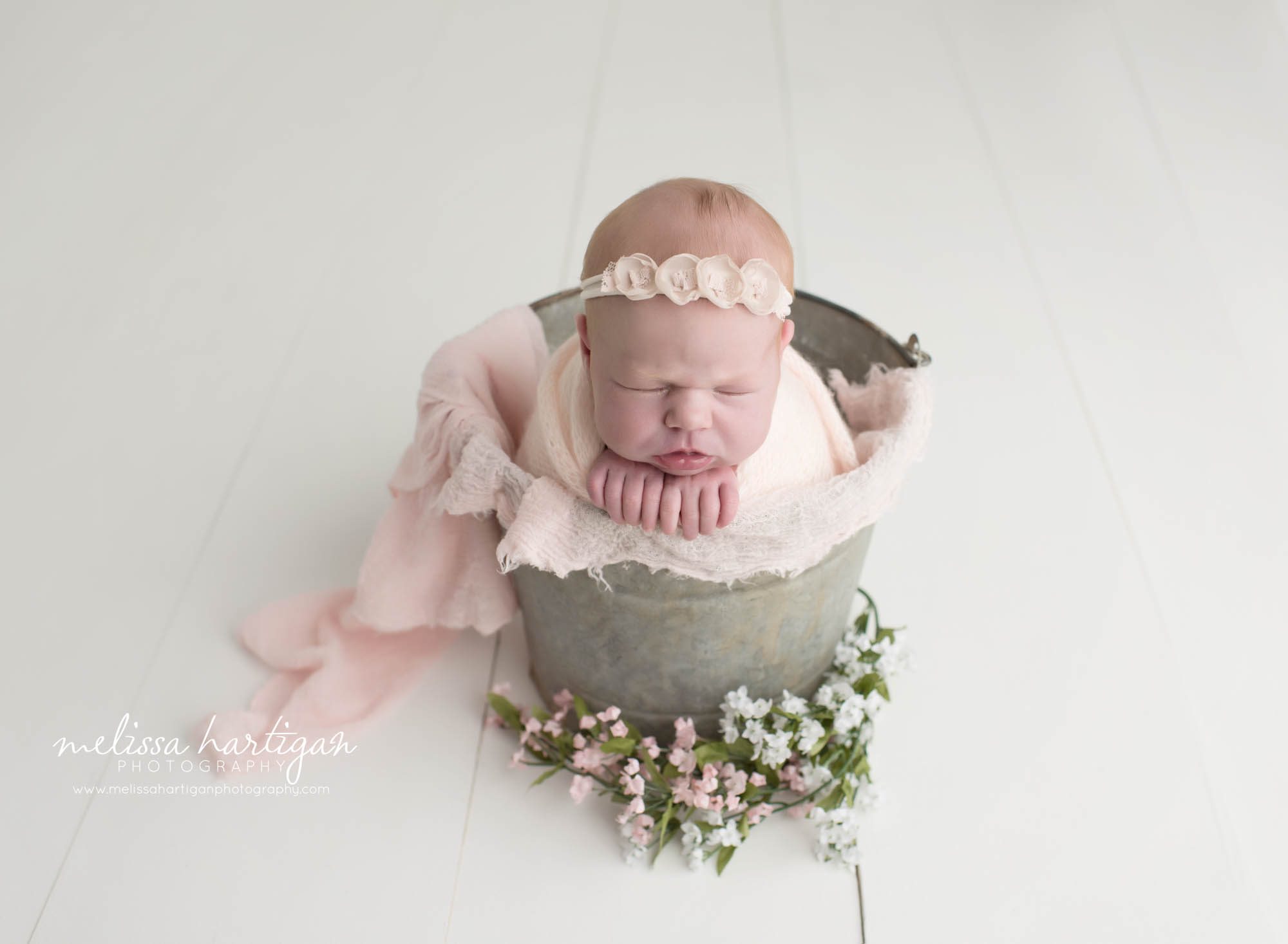 Melissa Hartigan Photography Connecticut Newborn Photographer in Coventry baby girl sleeping in metal bucket wrapped in pink with pink floral headband on white wooden floor