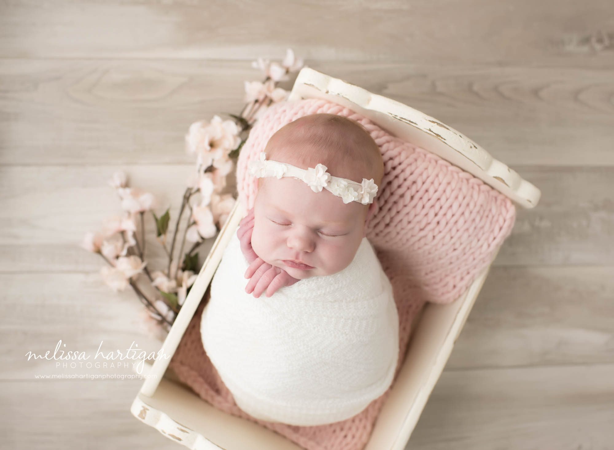 Melissa Hartigan Photography Connecticut Newborn Photographer in Coventry baby girl sleeping in white wooden bed wrapped in cream on pink blanket wearing white headband