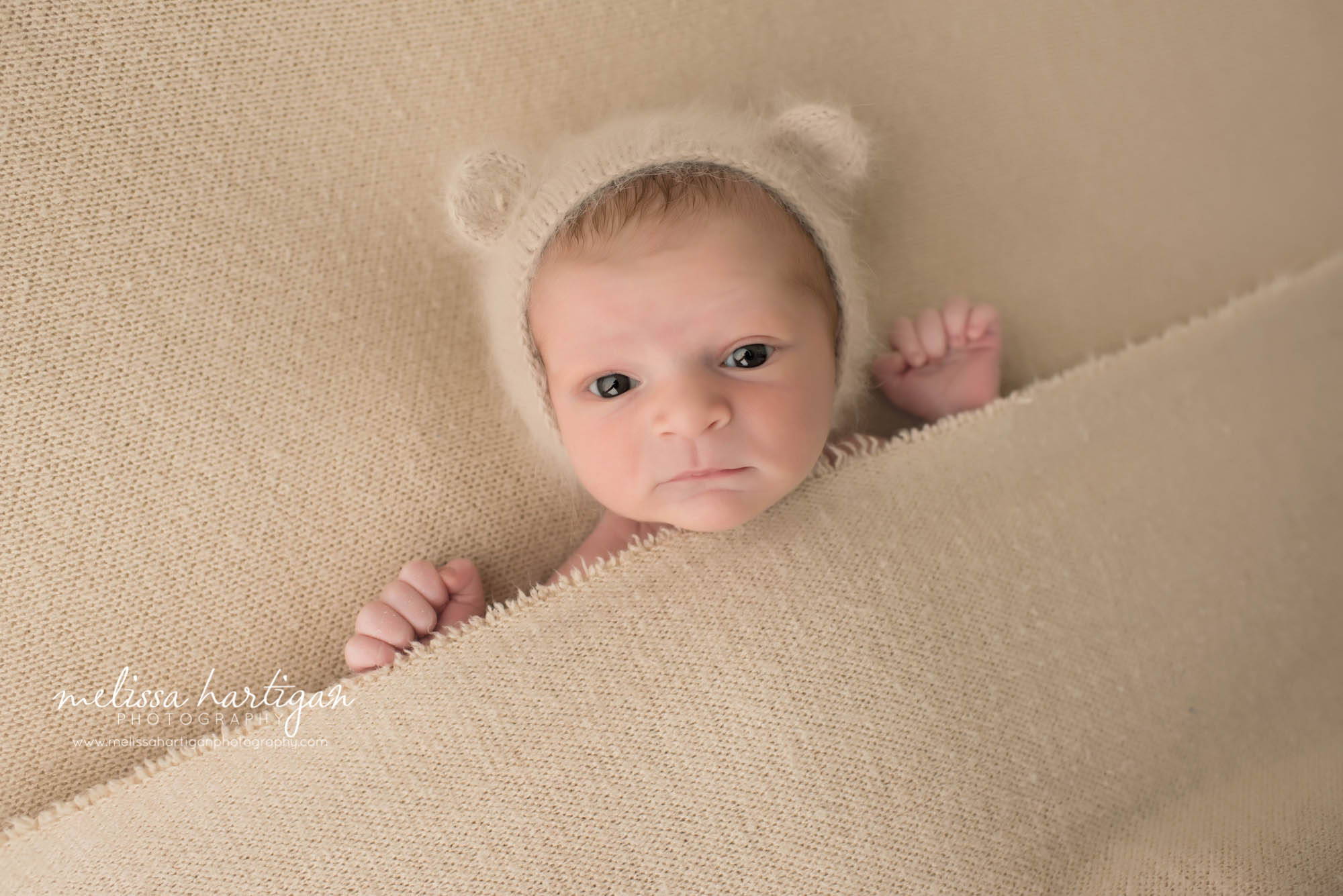 Melissa Hartigan Photography Newborn Photographer Connecticut baby boy wearing knit hat with ears laying under a tan knit blanket awake