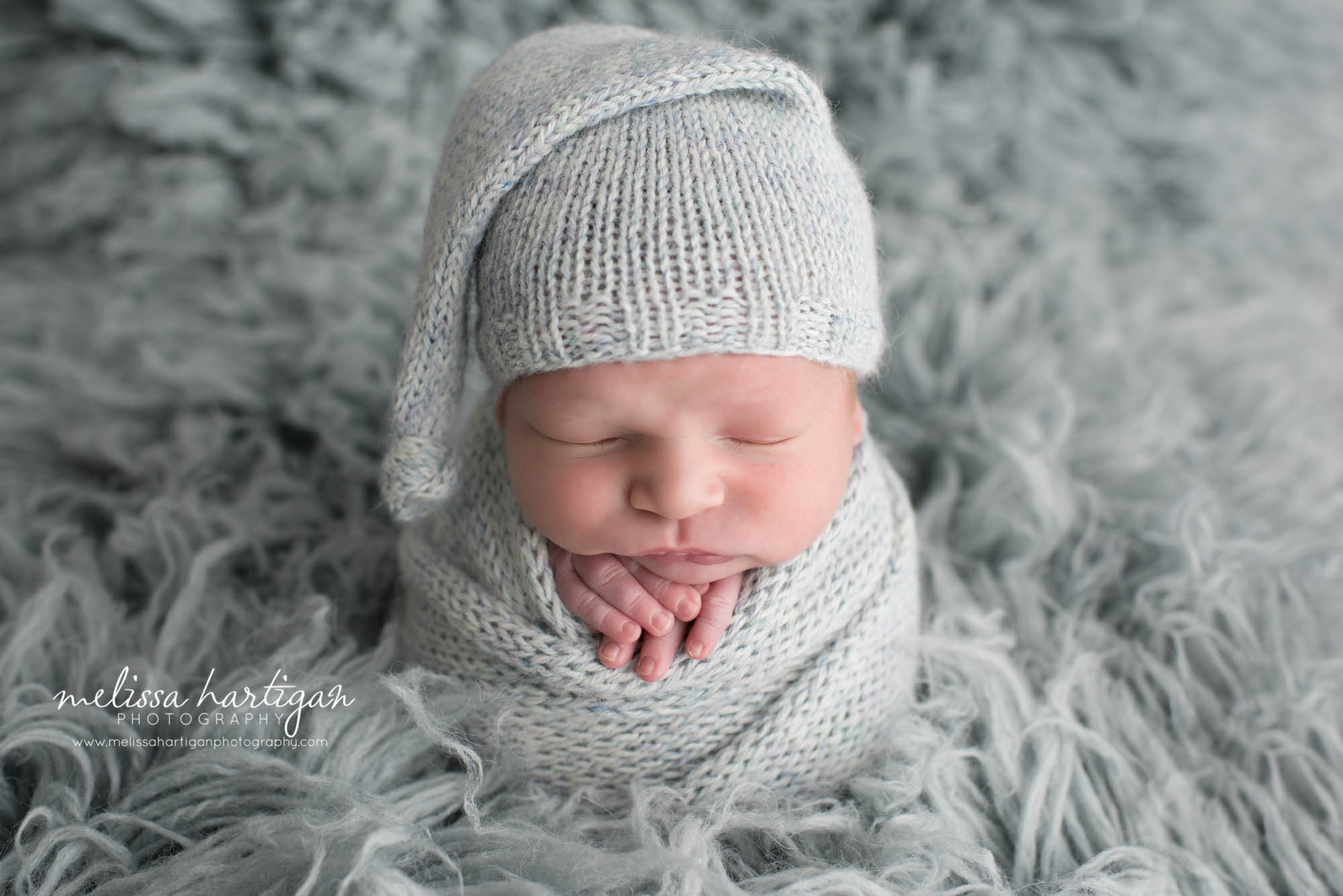 Melissa Hartigan Photography Newborn Photographer Connecticut baby boy wearing blue knit hat and matching wrap sleeping on a blue flokati rug