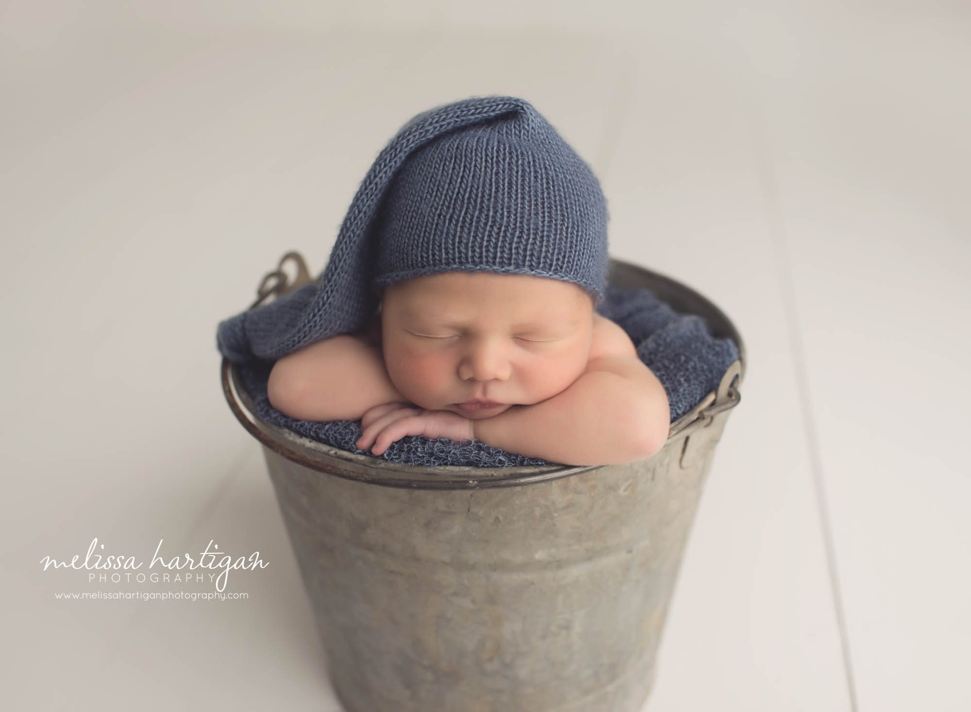 Melissa Hartigan Photography CT Newborn Photographer Braeden Newborn Session baby boy sleeping in metal bucket wearing blue knit hat and blue blanket