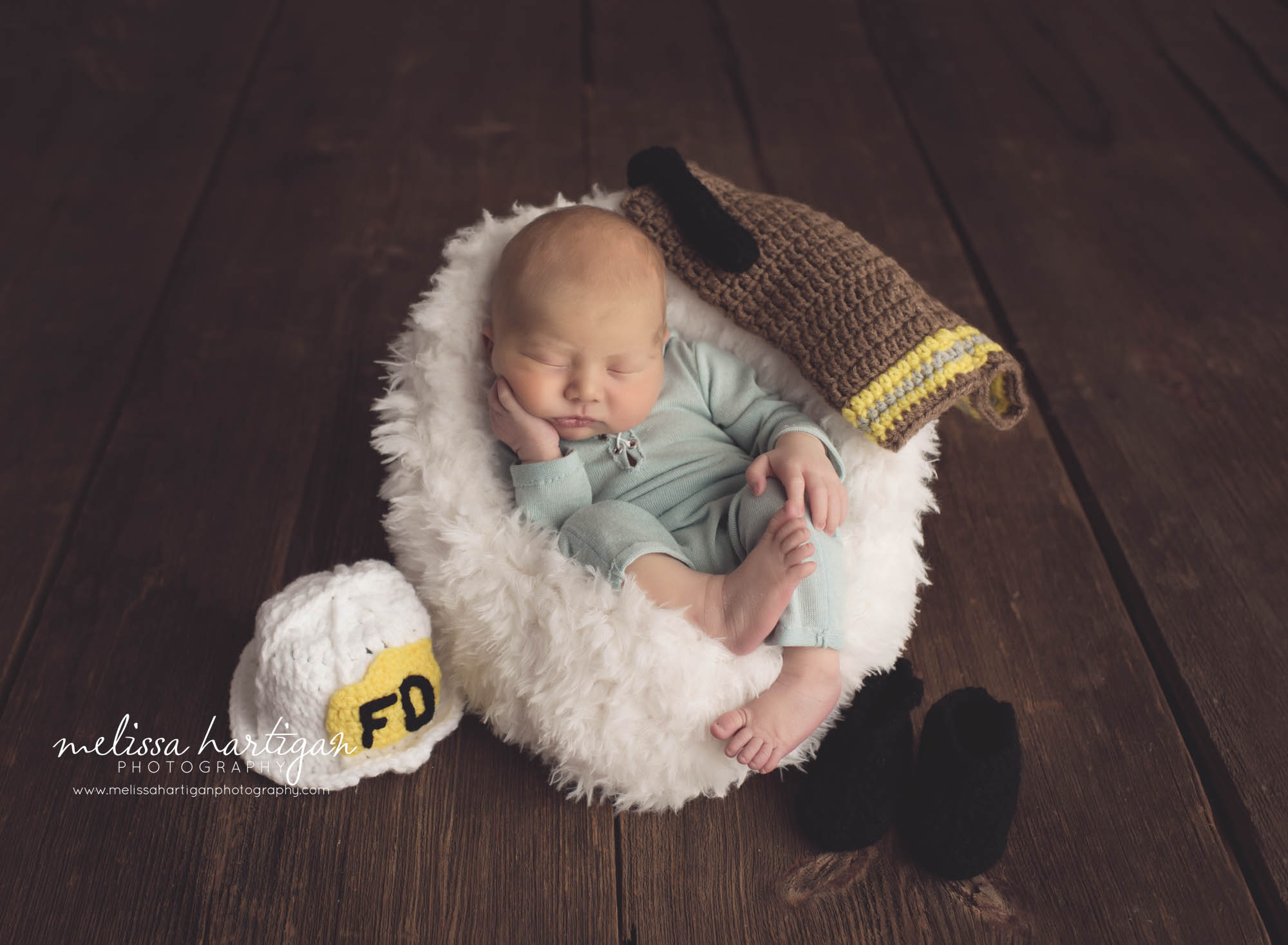 Melissa Hartigan Photography CT Newborn Photographer Braeden Newborn Session baby boy sleeping wearing knit blue onesie on fluffy white blanket with knit firefighter outfit placed around him