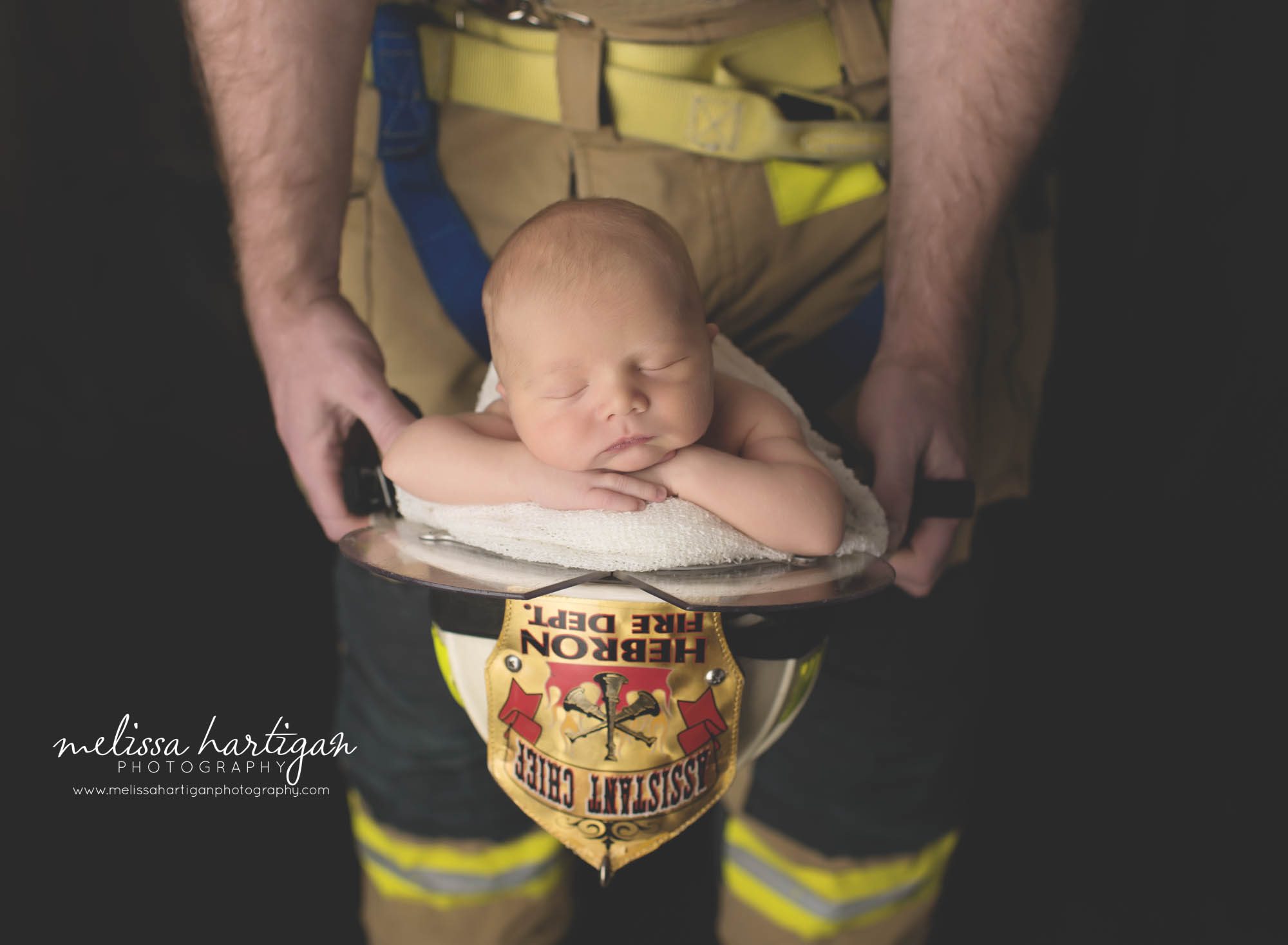 Melissa Hartigan Photography CT Newborn Photographer Braeden Newborn Session baby boy sleeping in father's firefight helmet dad stand behind in firefighter pants