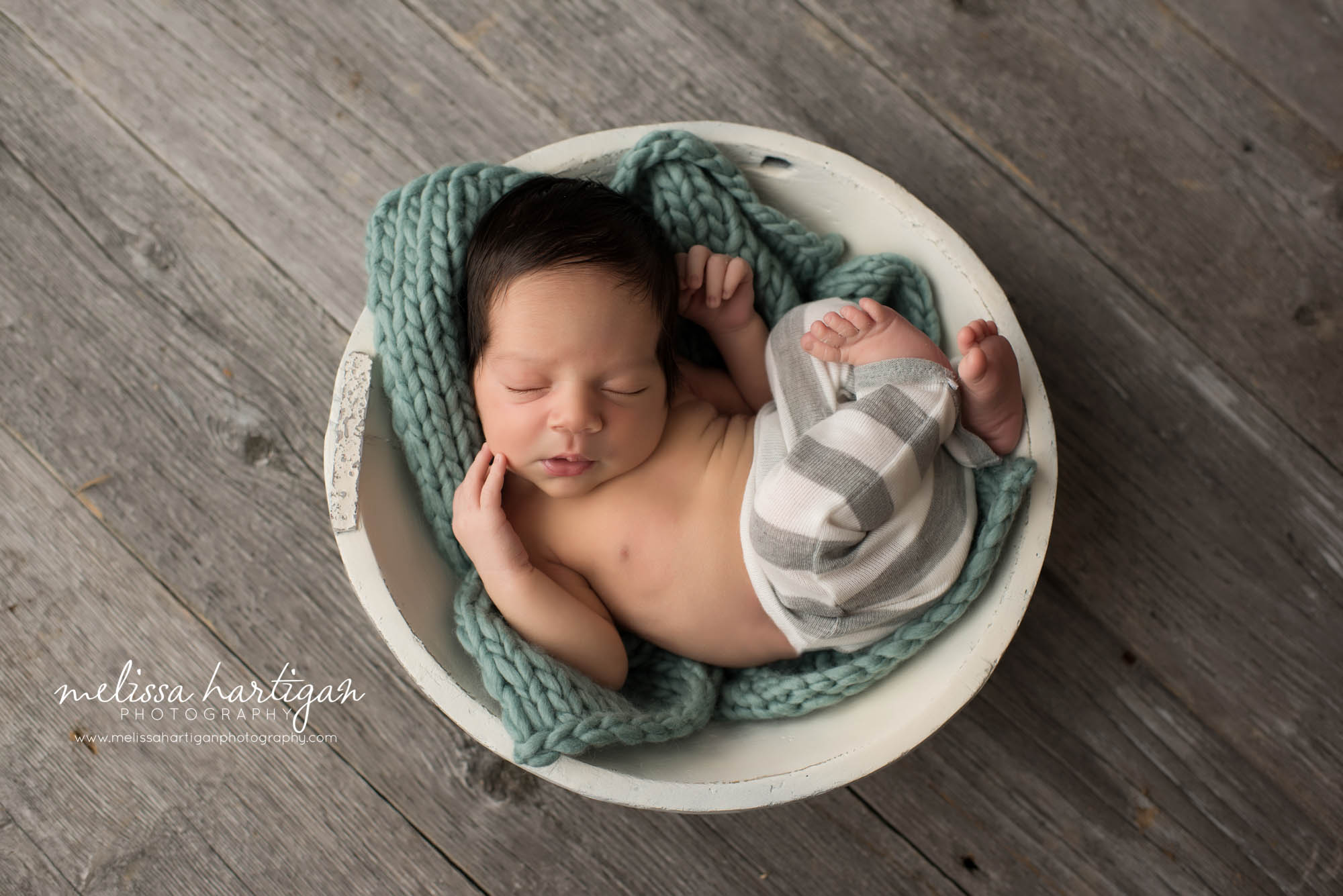 Melissa Hartigan Photography CT Newborn Photographer East Hartford baby boy sleeping in wooden white bowl on a teal knit blanket wearing gray and white striped pants