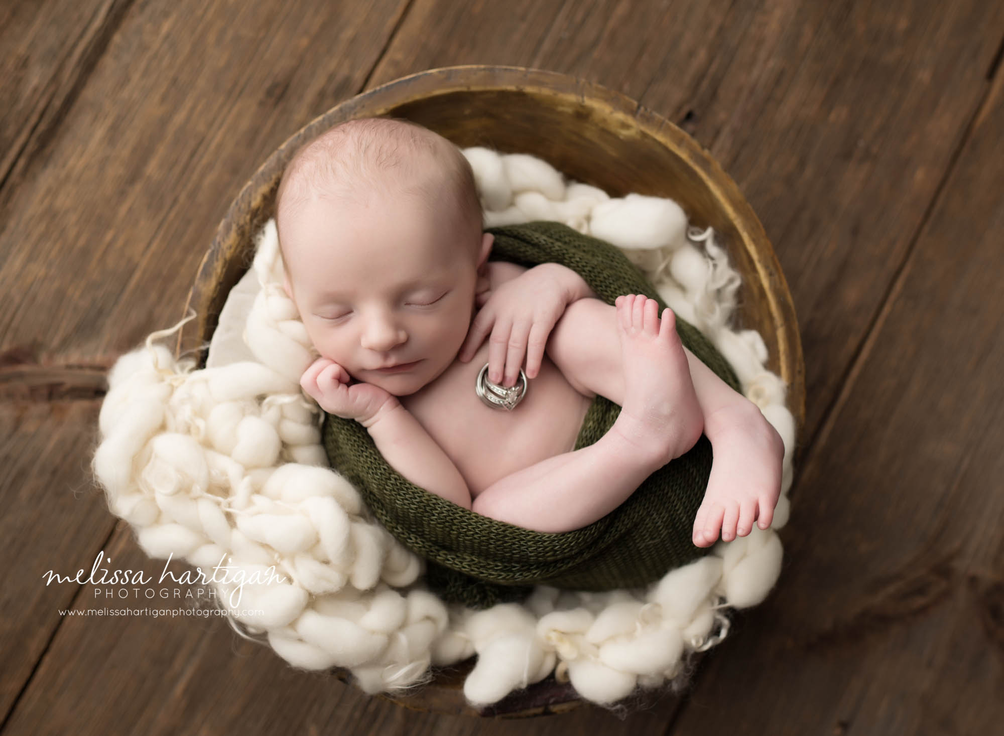 Melissa Hartigan Photography CT Newborn Photographer Stafford baby boy sleeping in wooden bowl with white chunky knit blanket in green wrap holding parent's wedding rings 