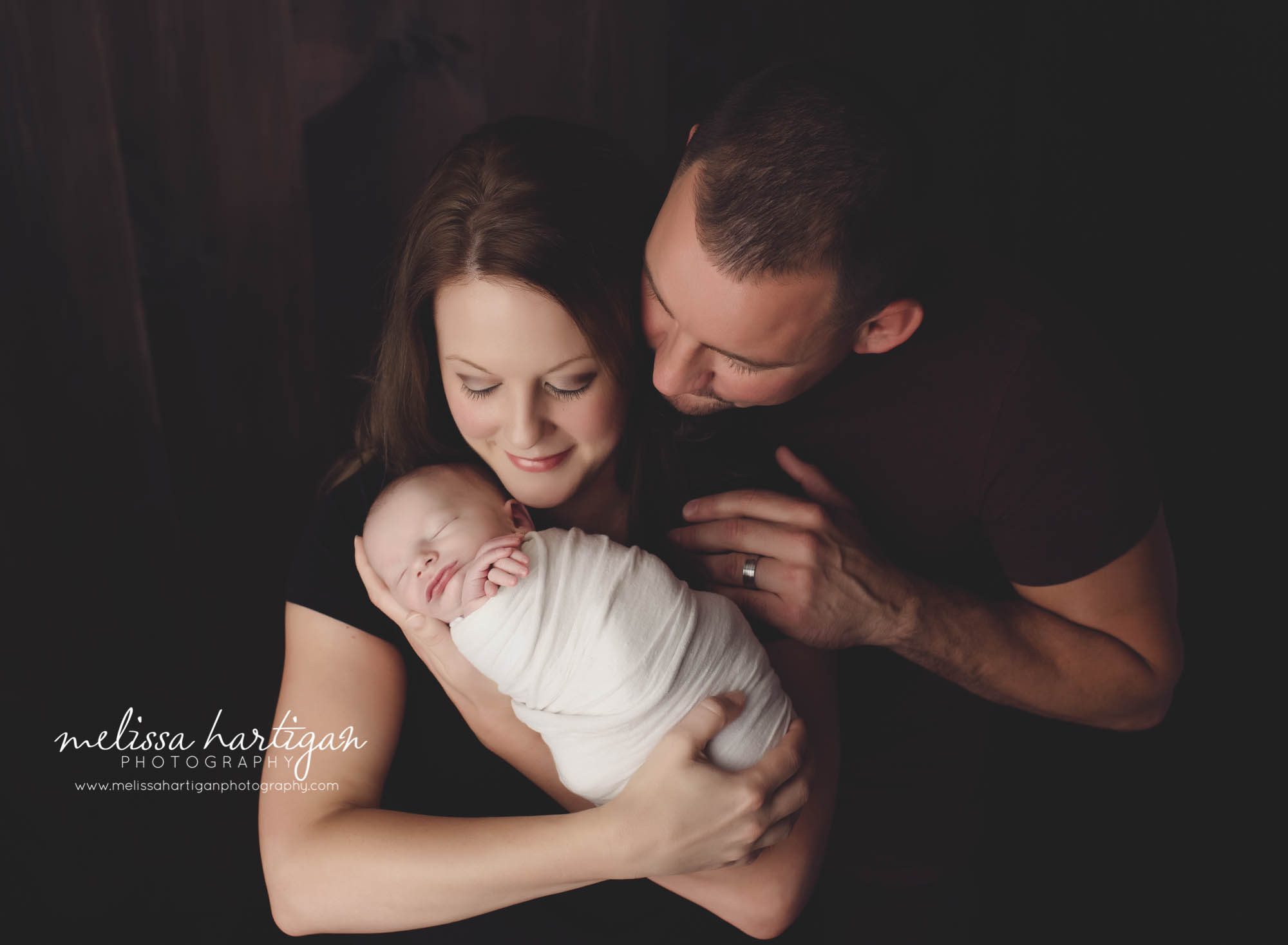 Melissa Hartigan Photography CT Newborn Photographer Stafford baby boy sleeping wrapped in cream held my mother with father looking over her shoulder at baby