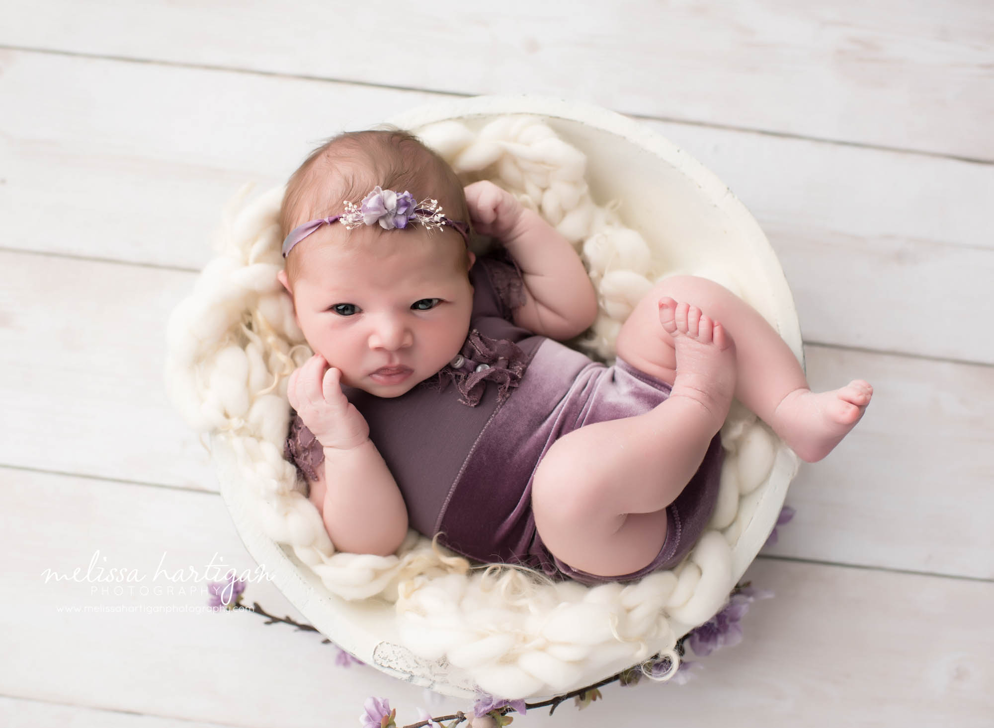 Melissa Hartigan Photography CT Newborn Photographer Ashford baby girl awake wearing purple velvet onesie and floral headband in white wooden bowl