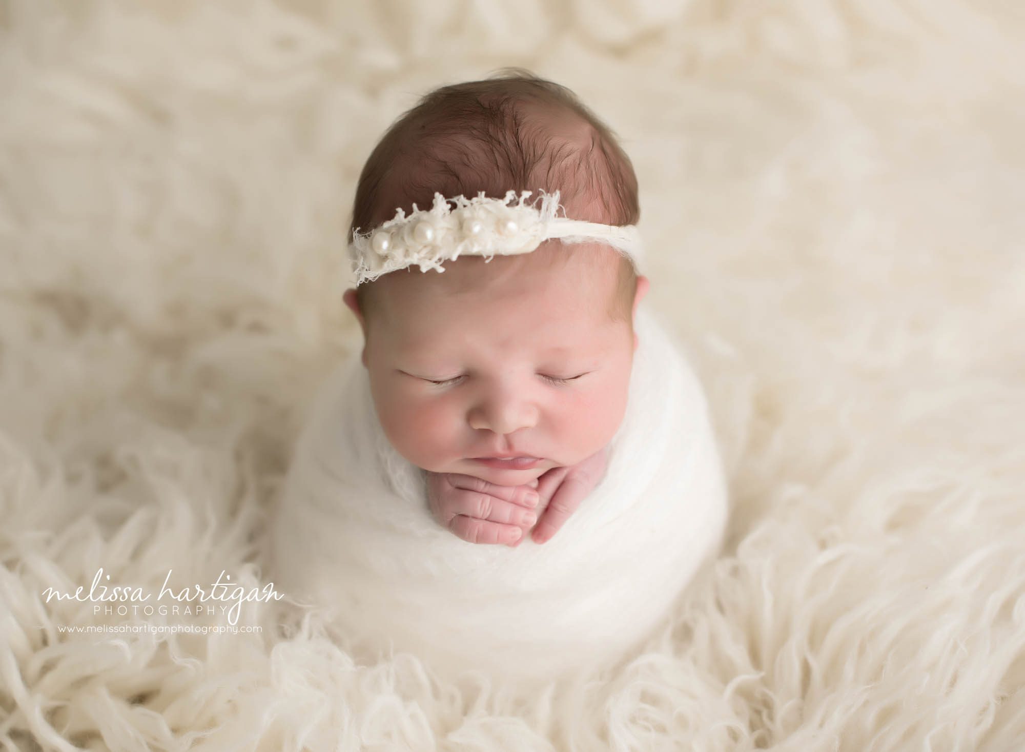 Melissa Hartigan Photography CT Newborn Photographer Ashford baby girl sleeping wrapped in cream with hands sticking out wearing cream floral headband on white flokati rug