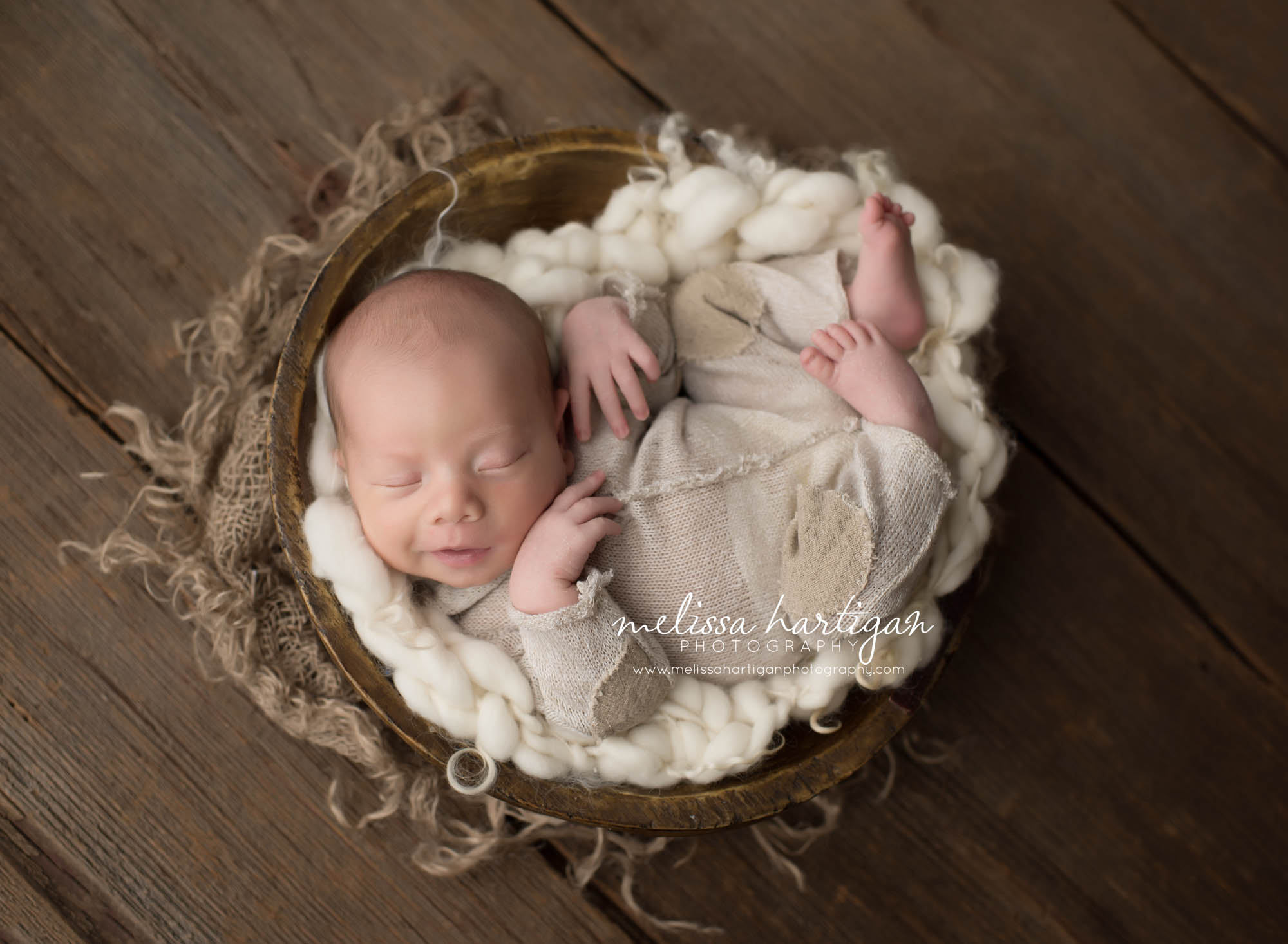 Melissa Hartigan Photography CT Newborn Photographer Taave CT Newborn Session baby boy wearing cream knit onesie sleeping in a wooden bowl with chunky white knit blanket smiling