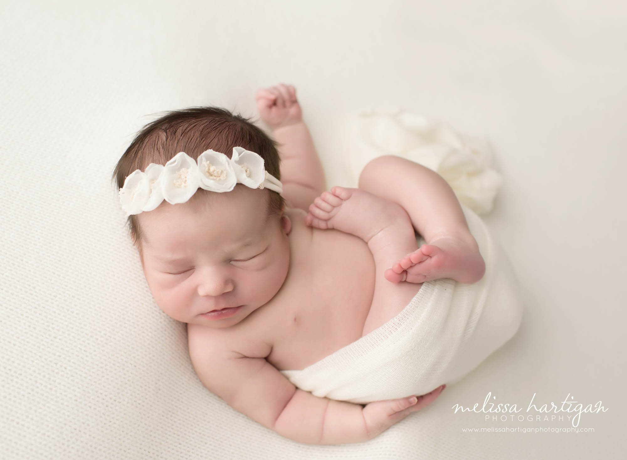 Melissa Hartigan Photography CT Newborn Photographer Emerson CT Newborn Session baby girl sleeping with tushy wrapped in white blanket wearing white floral headband with arms and feet untucked