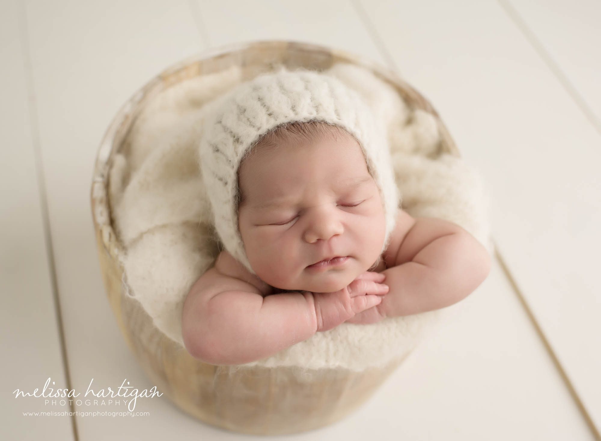 Melissa Hartigan Photography CT Newborn Photographer Emerson CT Newborn Session baby girl sleeping in wooden bucket with cream blanket and knit hat with arms crossed under chin