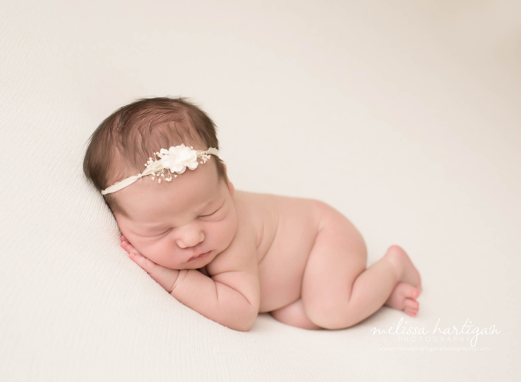 Melissa Hartigan Photography CT Newborn Photographer Emerson CT Newborn Session baby girl sleeping with hands tucked under cheek on cream blanket wearing white floral headband