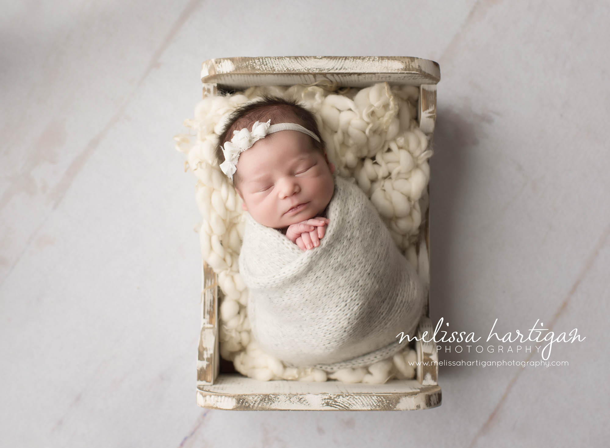 Melissa Hartigan Photography CT Newborn Photographer Emerson CT Newborn Session baby girl sleeping in white wooden bed wrapped in cream knit with white floral headband