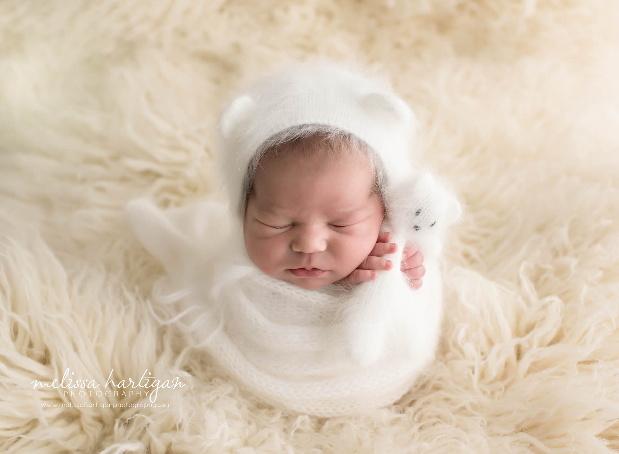 Melissa Hartigan Photography CT Newborn Photographer Emerson CT Newborn Session baby girl sleeping wrapped in white wrap with matching white knit hat with ears on white fluffy rug holding white knit bear