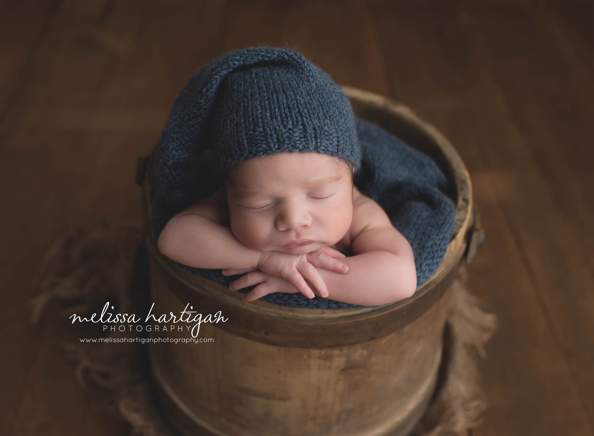CT Newborn Photographer baby boy sleeping in wooden bucket wearing blue knit hat 