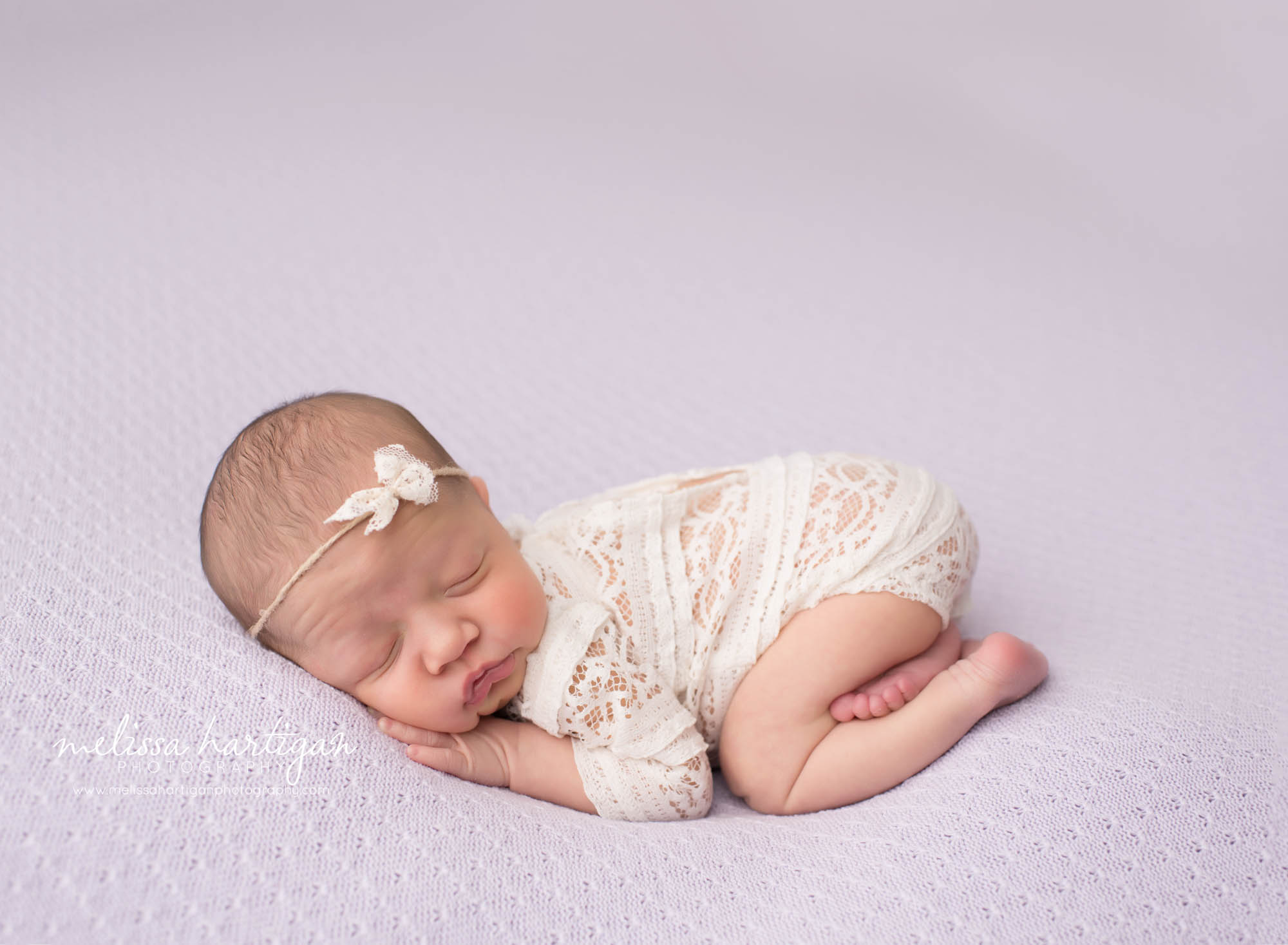 Baby girl wearing lace romper posed bum up on light purple blanket newborn pictures from baby studio session