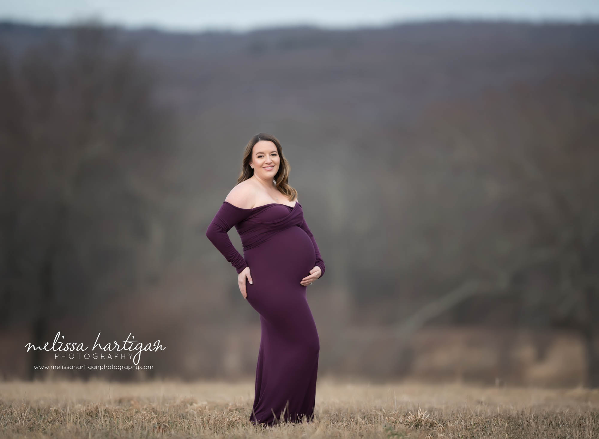 expectant mom smiling and standing for pregnancy pose flattering baby bump winter maternity photos with no snow