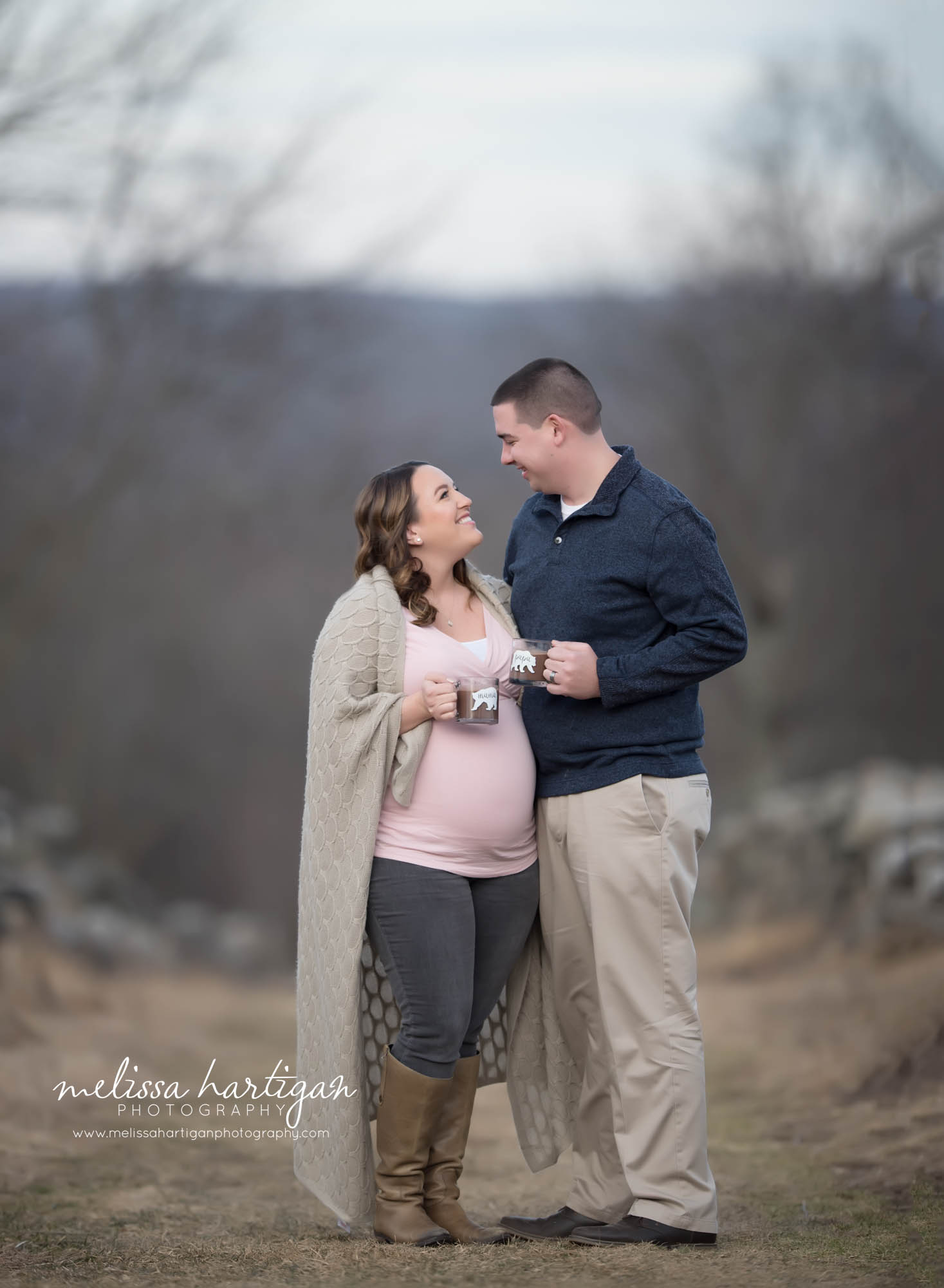 Expectant couple standing looking at eachother connected maternity pose holding mugs with hot chocolate winter maternity pictures with no snow CT maternity newborn photography session