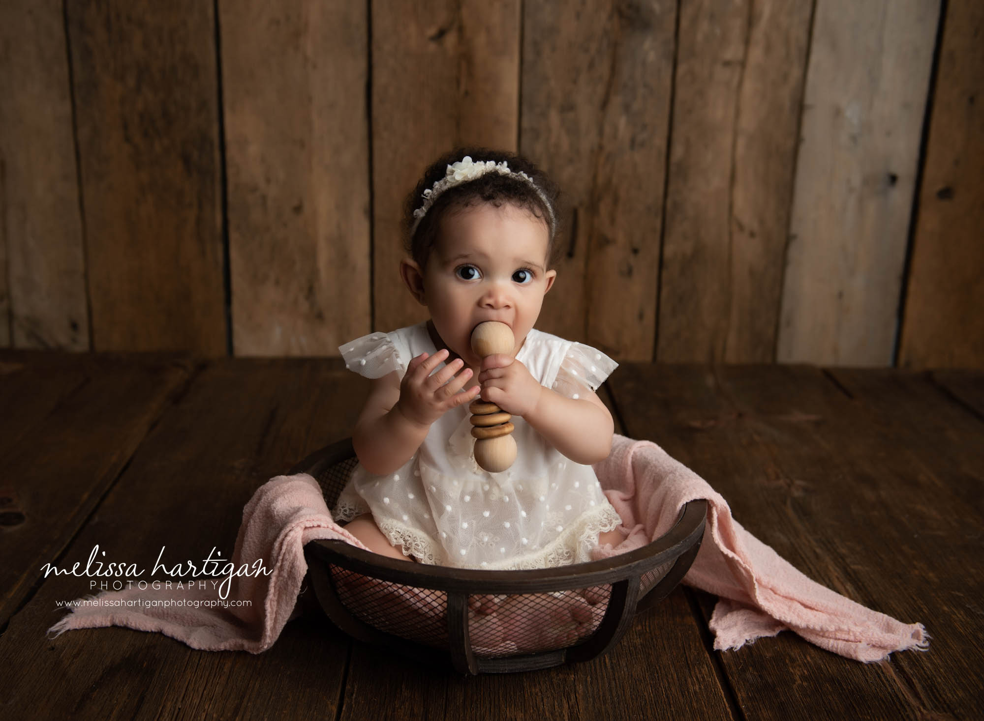 Milestone photography session cream dress with muted pink layer wooden baby rattle and rustic wooden boards baby photography Connecticut photographer melissa hartigan