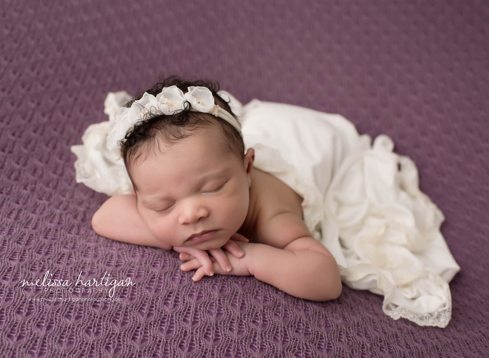 baby girl on purple with cream blanket draped over her posed with head on hands