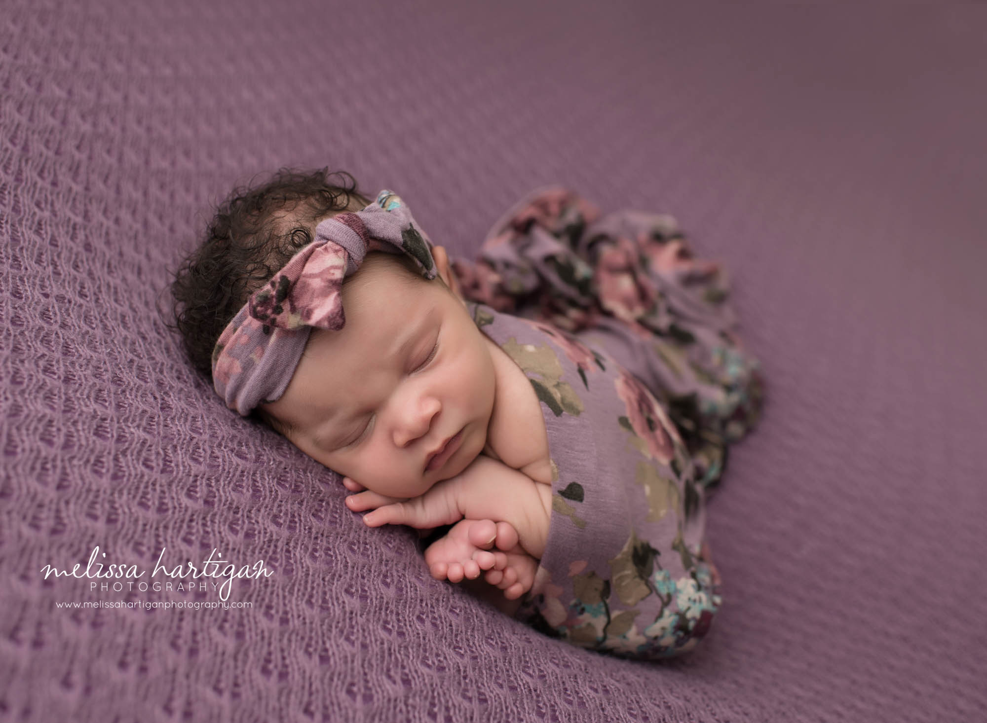 baby girl posed with muted purple toned floral wrap and bow headband