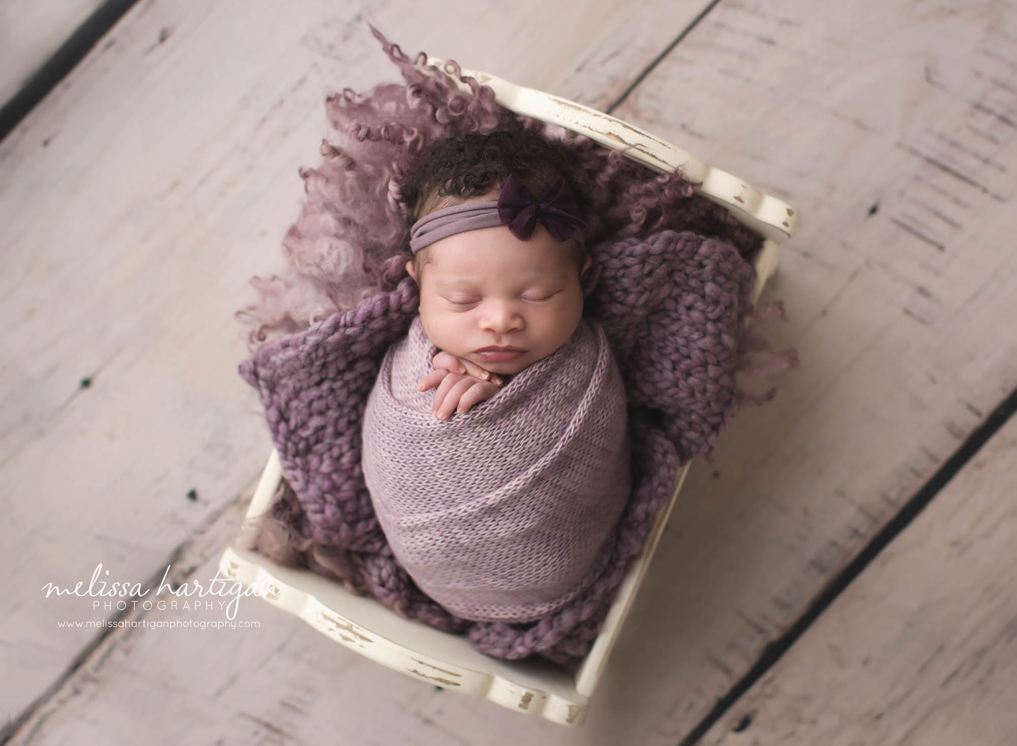 baby girl posed in cream cradle prop wrapped in purple toned knitted wrap and purple curly layers and chuncky knit blanket newborn photography Middletown Haddem CT