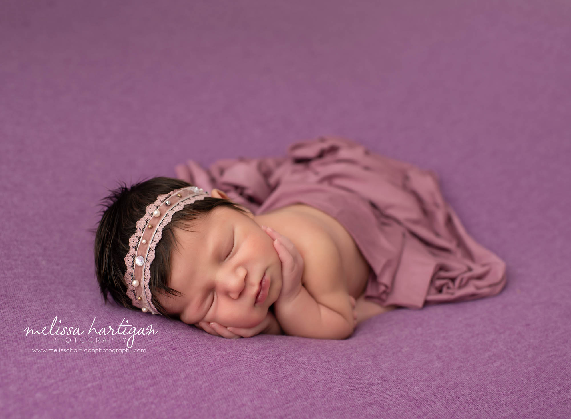 Baby girl laying on side with hands under chin purple blanket and deep mauve layer