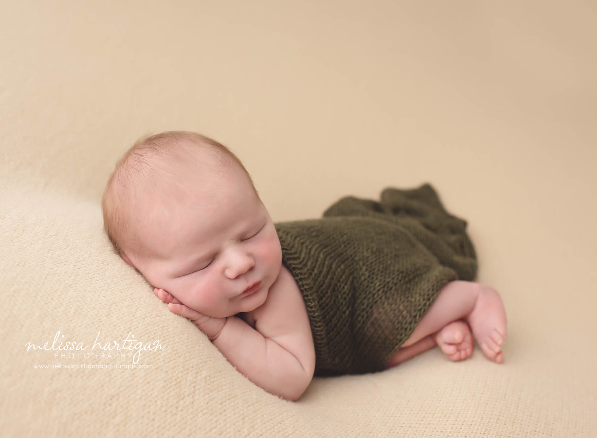 newborn posed side laying with green wrap on cream textured blanket