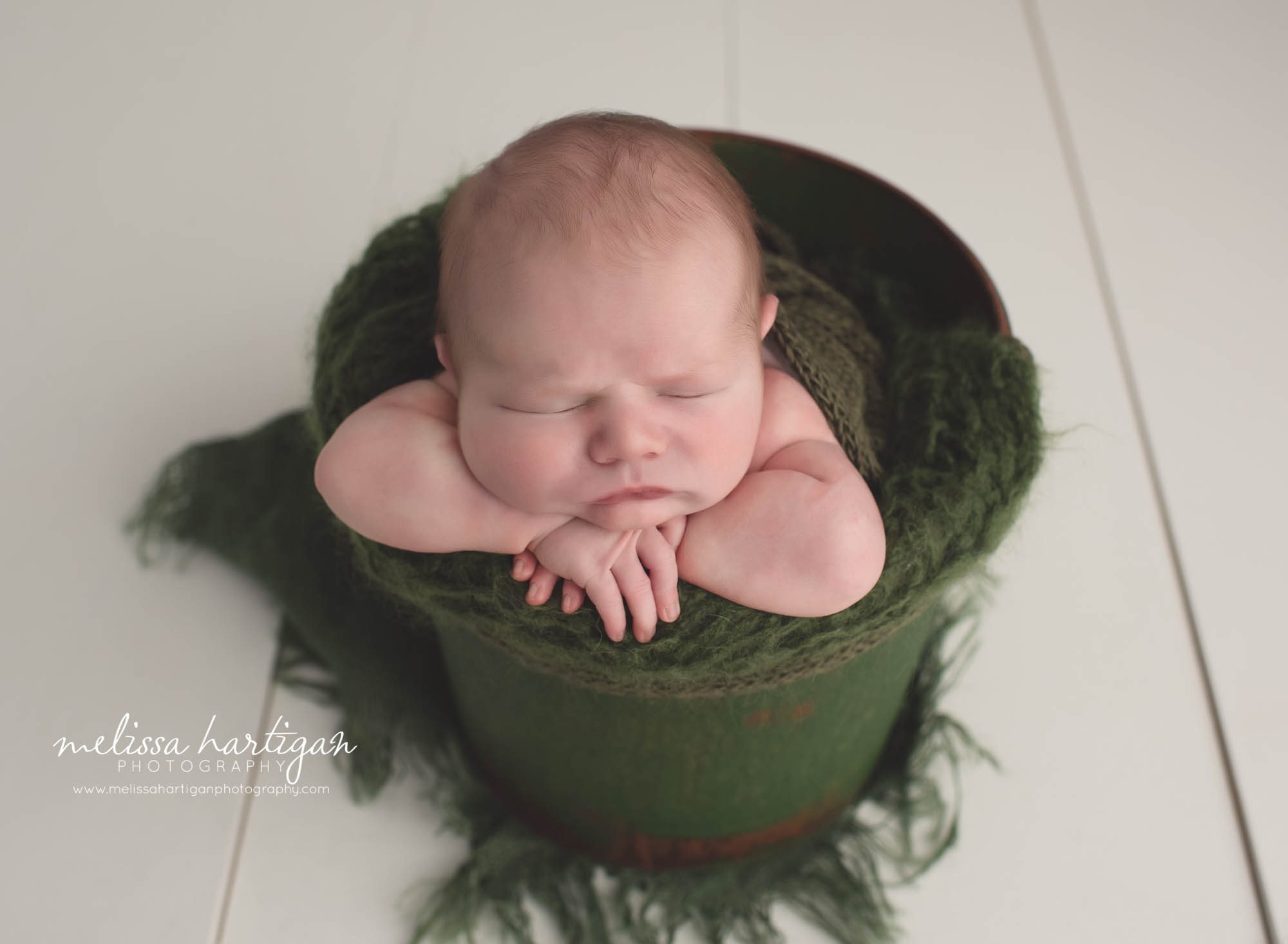 baby boy posed in green bucket with green layers head on hands Baby photography in CT