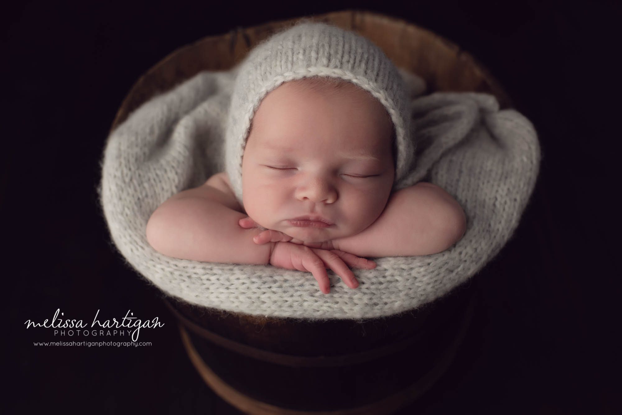 newborn baby posed in bucket with neutral color knitted wrap and bonnet