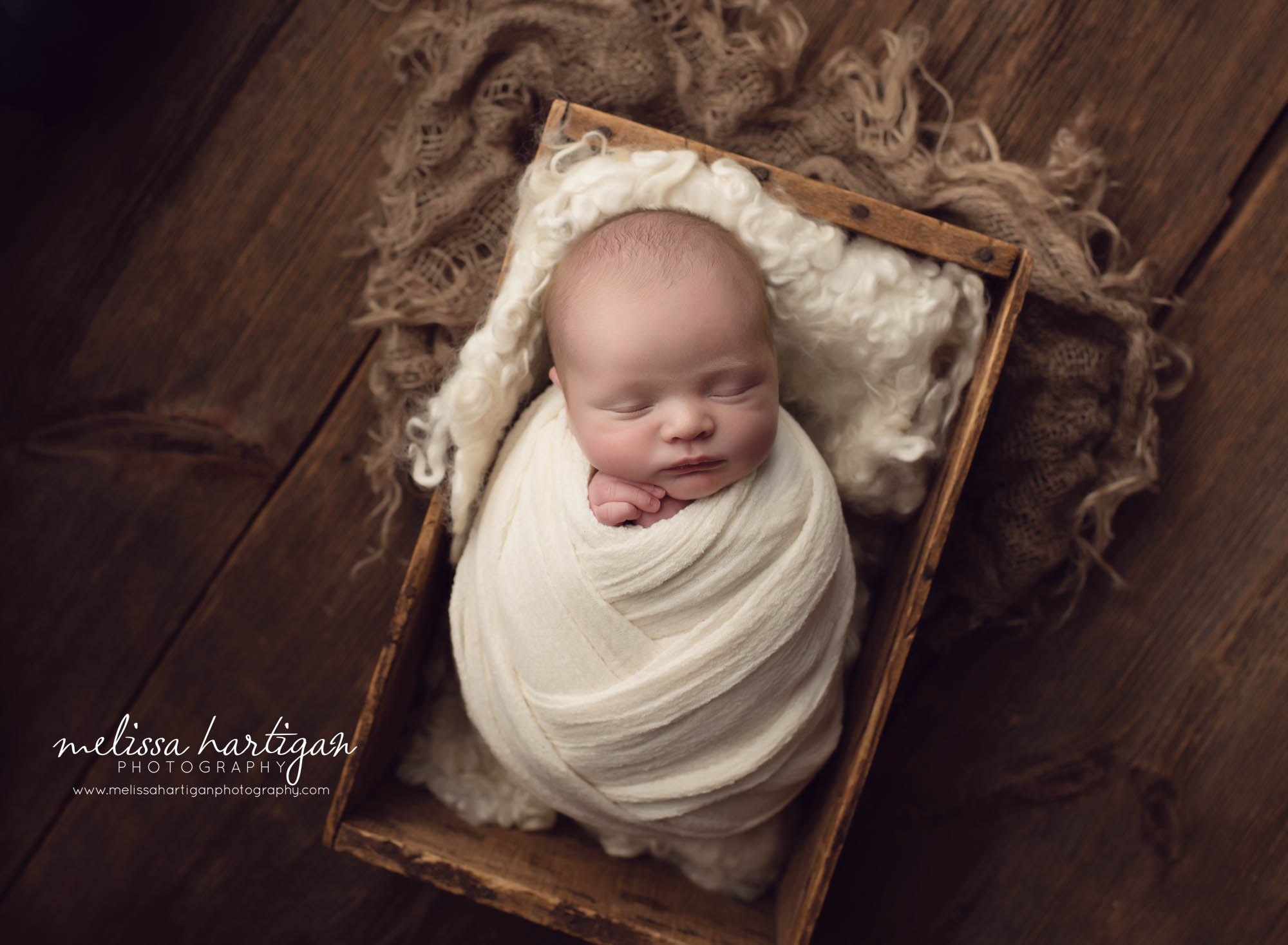 baby wrapped in cream layered wrap in a create with burlap on wood boards