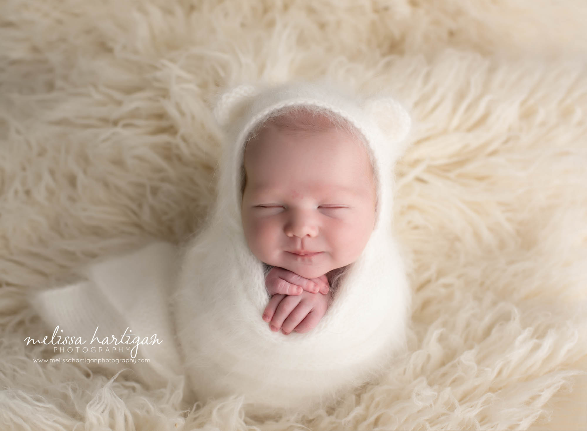 Newborn baby wrapped in knitted white wrap with knitted bear bonnet