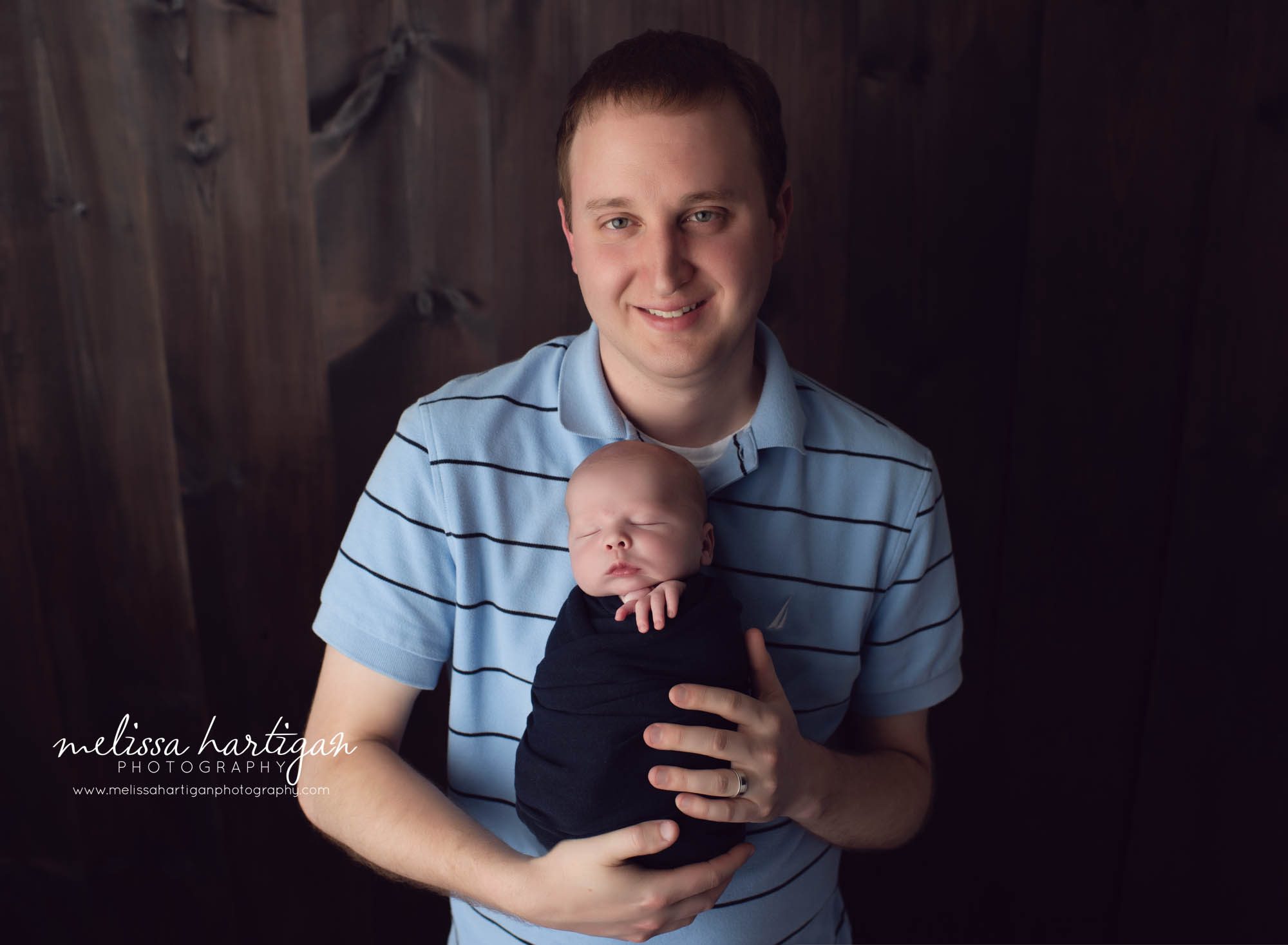 Dad pose with newborn baby wrapped in navy color